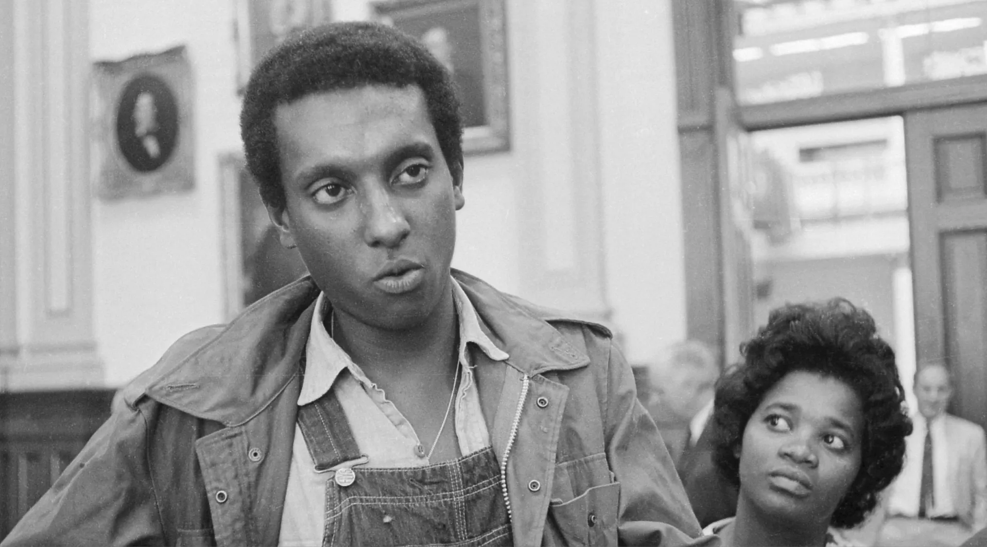 Stokely Carmichael speaking passionately during a civil rights meeting, with a woman looking on beside him.