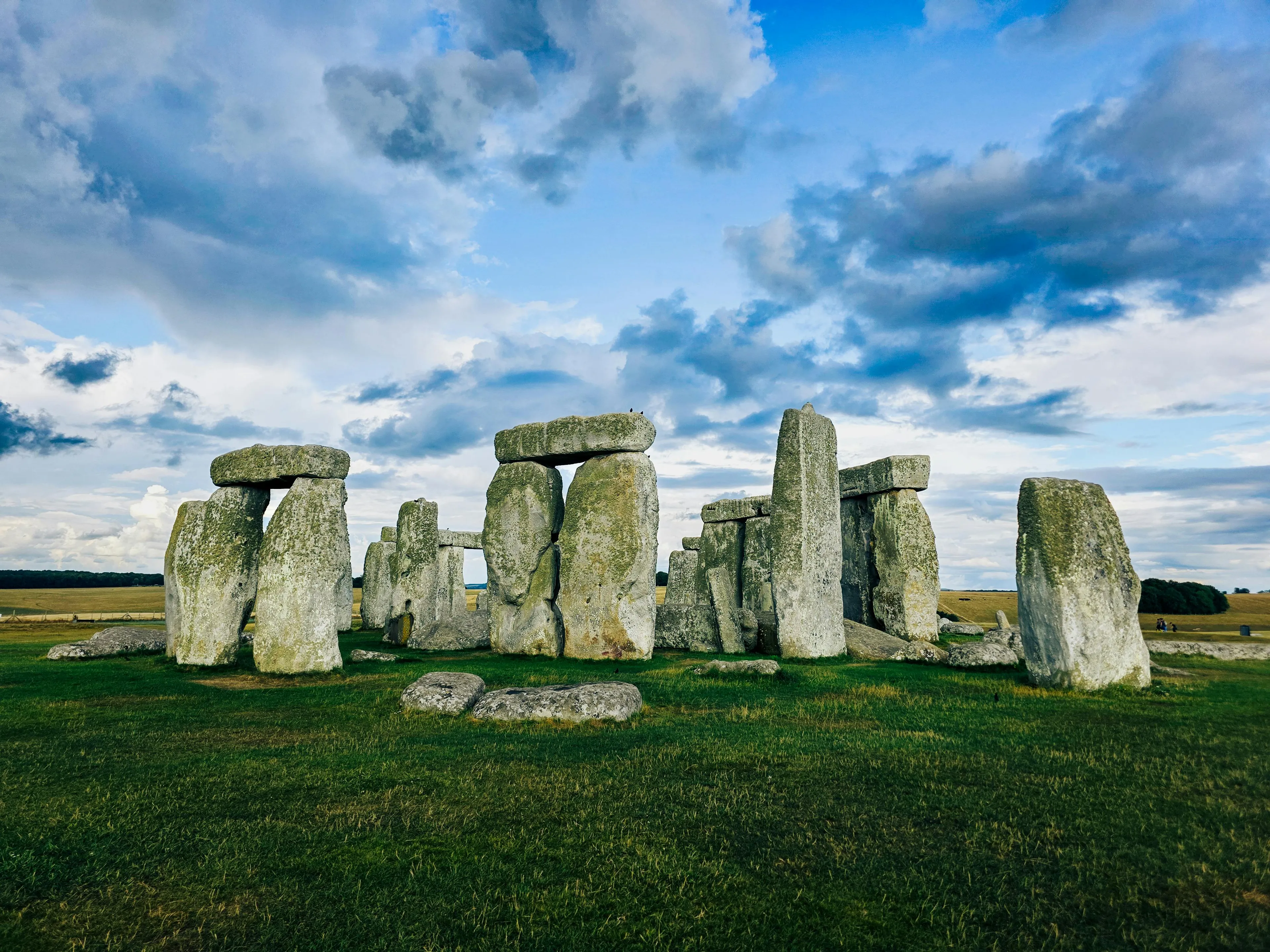 Stonehenge standing tall on green grass under a partly cloudy blue sky, a famous ancient landmark.