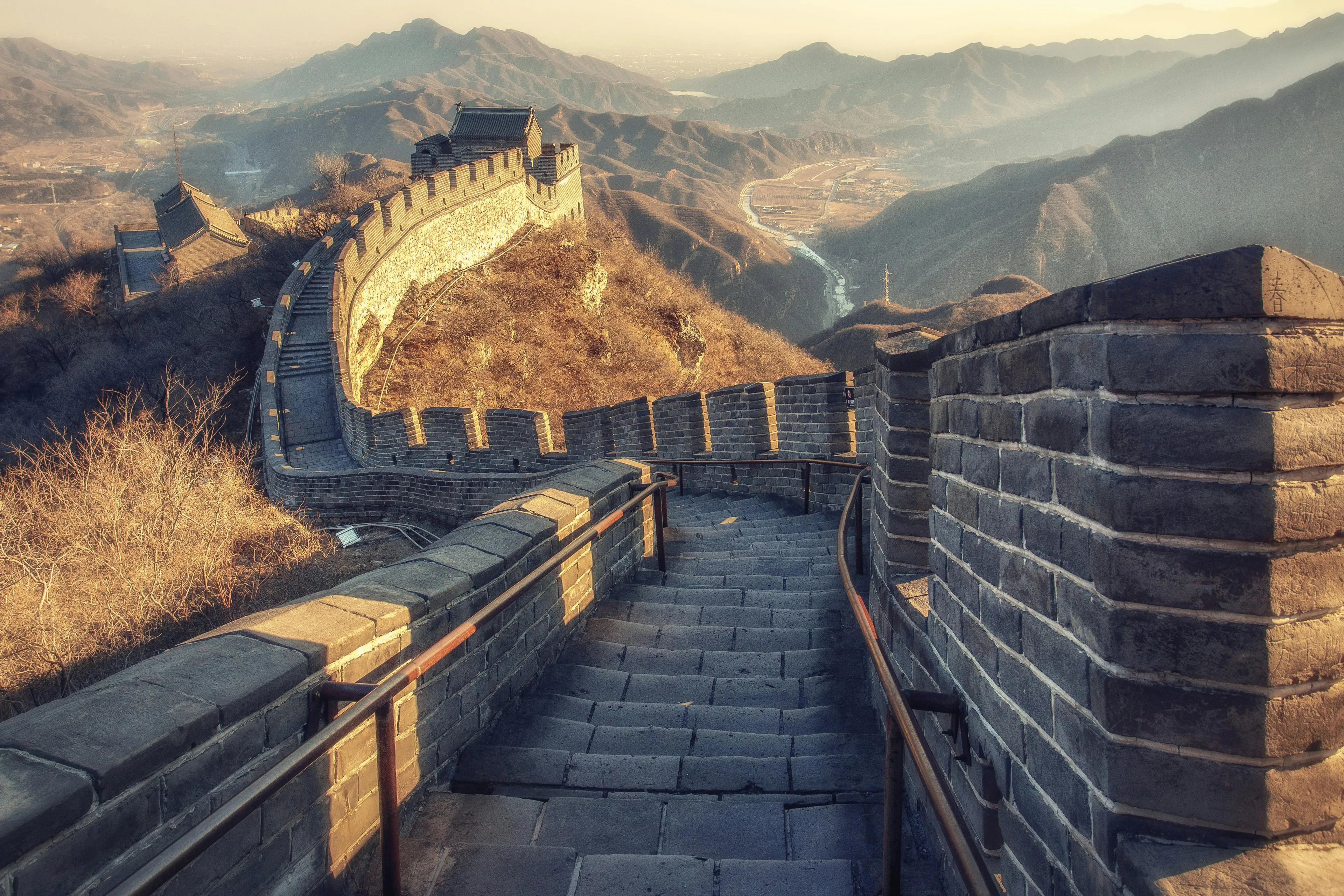 The Great Wall of China winding through mountainous landscape under soft sunlight.