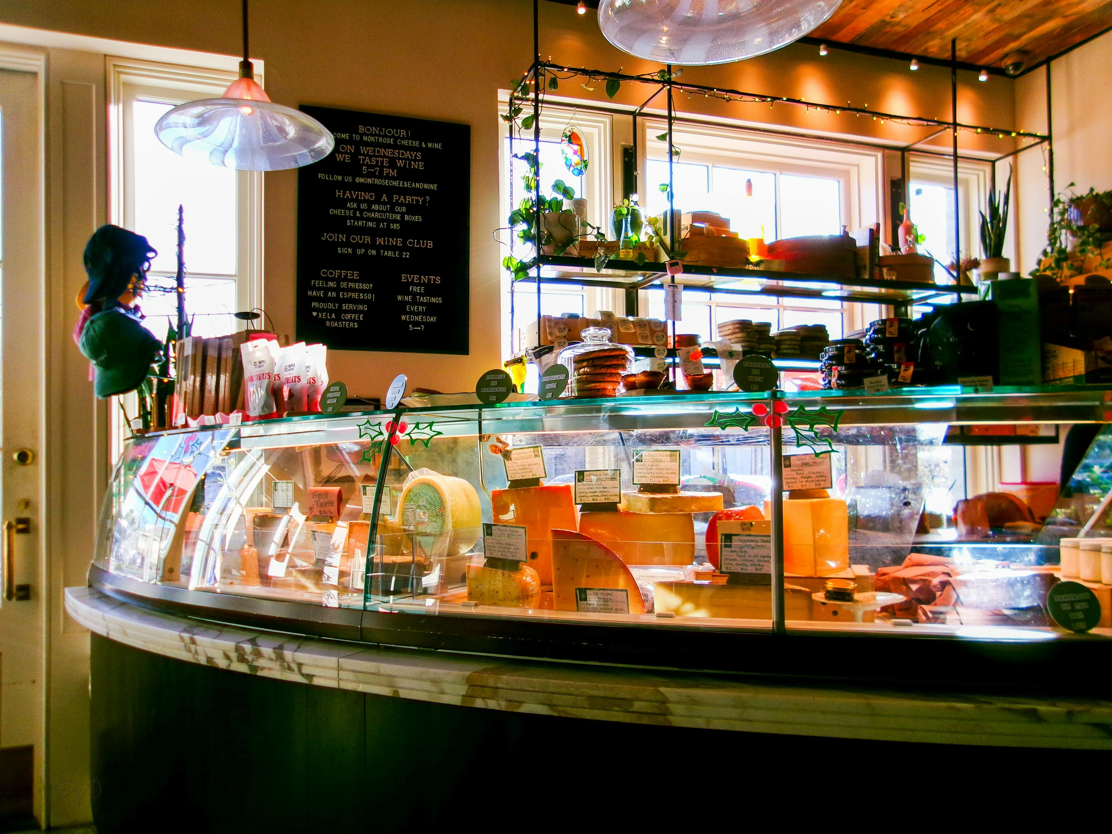 Interior of a neighborhood wine and cheese shop with a glass display case filled with various cheeses.