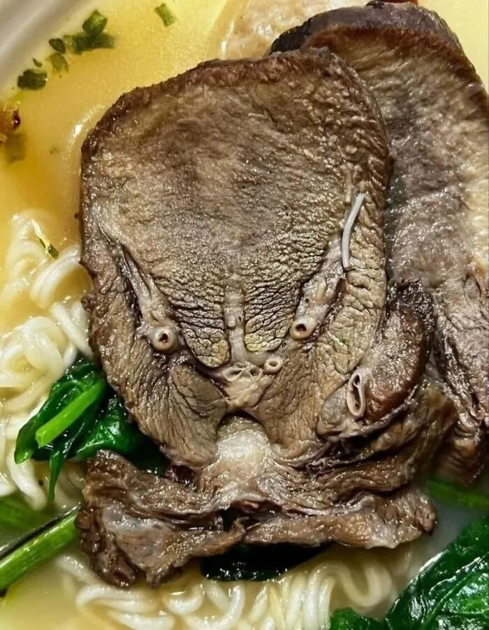 Close-up of a mushroom in ramen noodles resembling a face, illustrating pareidolia in food photography.