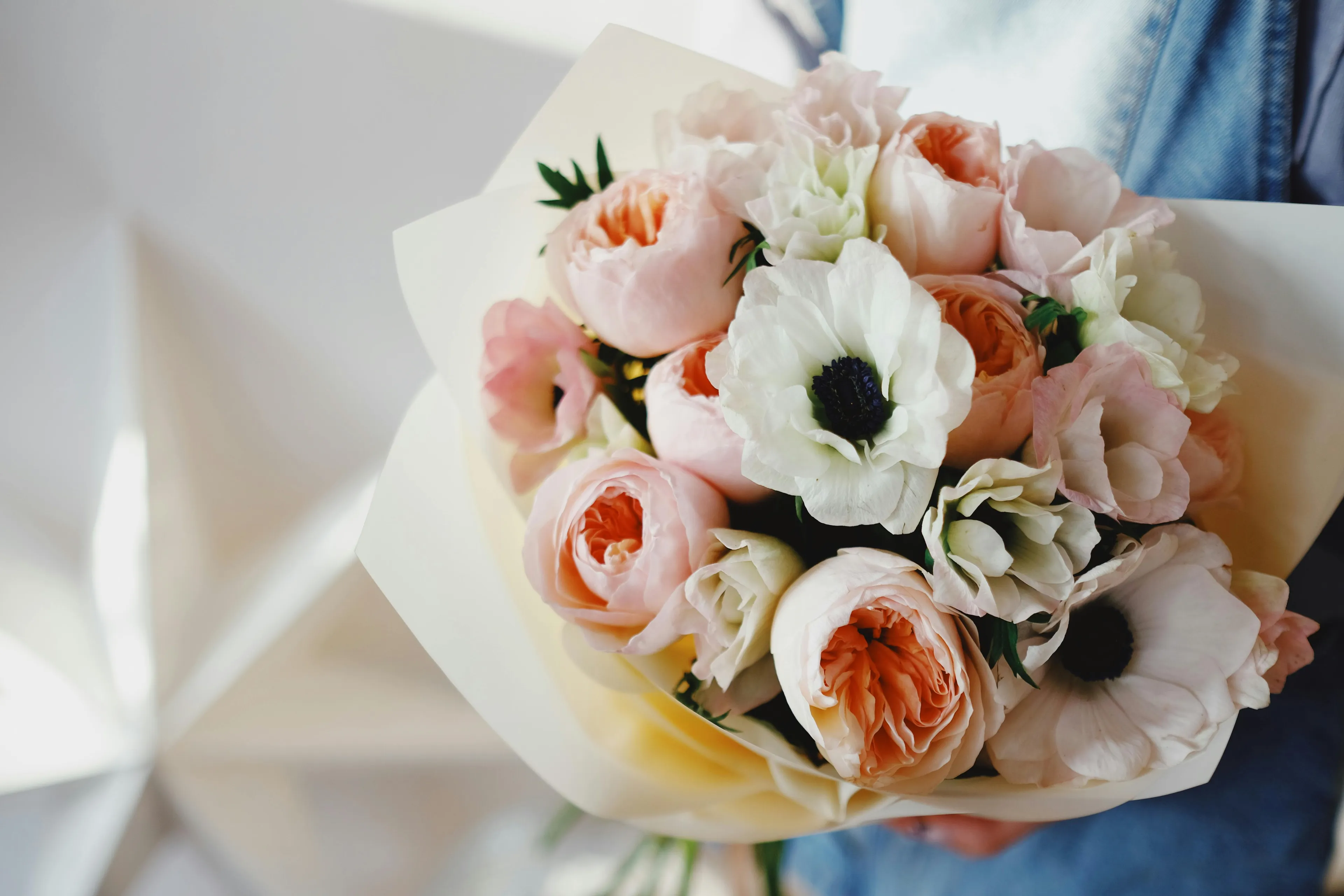 A bouquet of their favorite flowers held by a person, featuring peach roses and white anemones wrapped in paper.