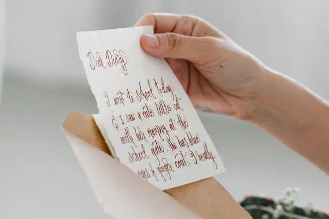 Hand holding a handwritten letter being pulled out of an envelope, a surprise gift for a friend.