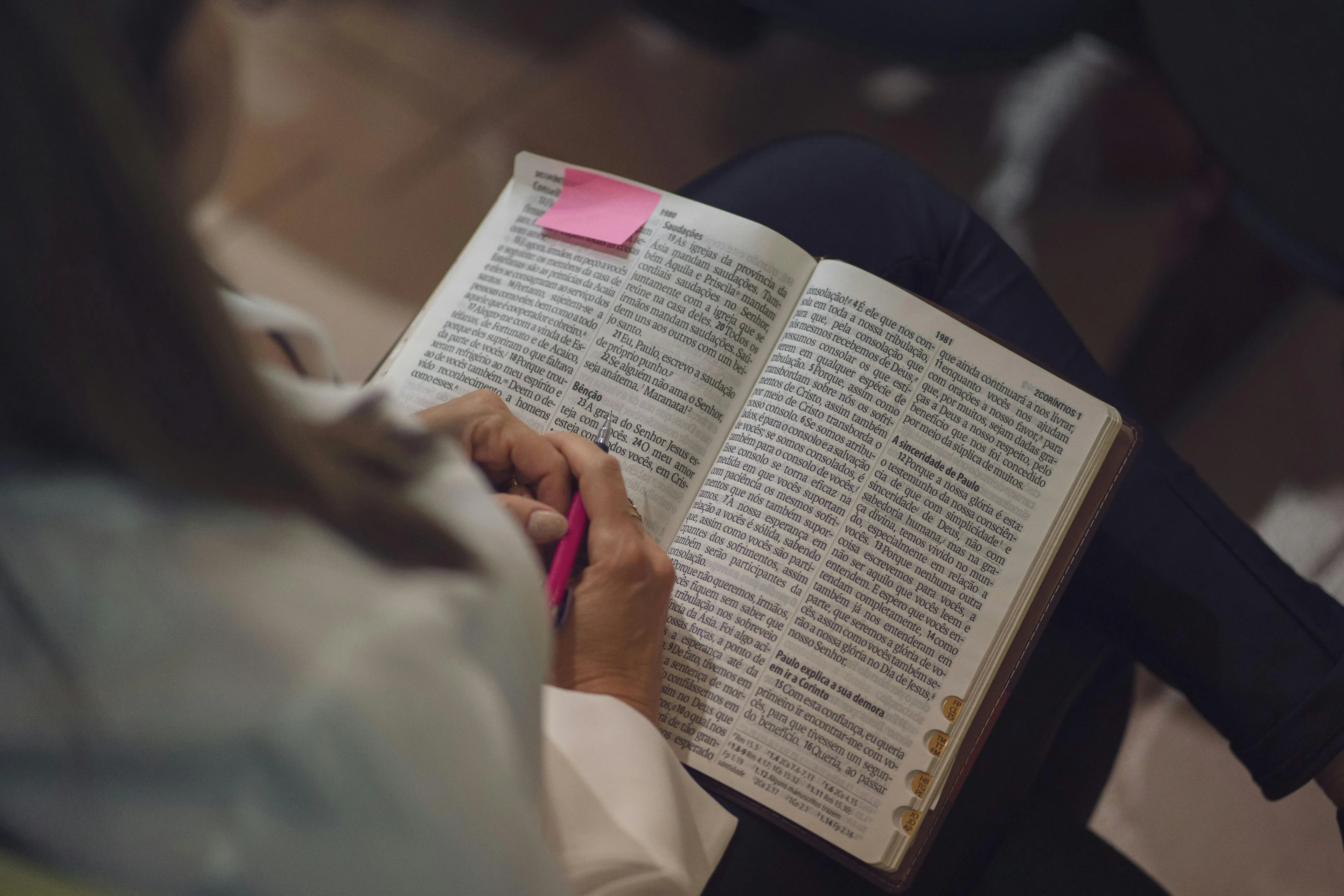 Person holding a book with notes and a pink bookmark, highlighting text, a thoughtful surprise gift idea for a friend