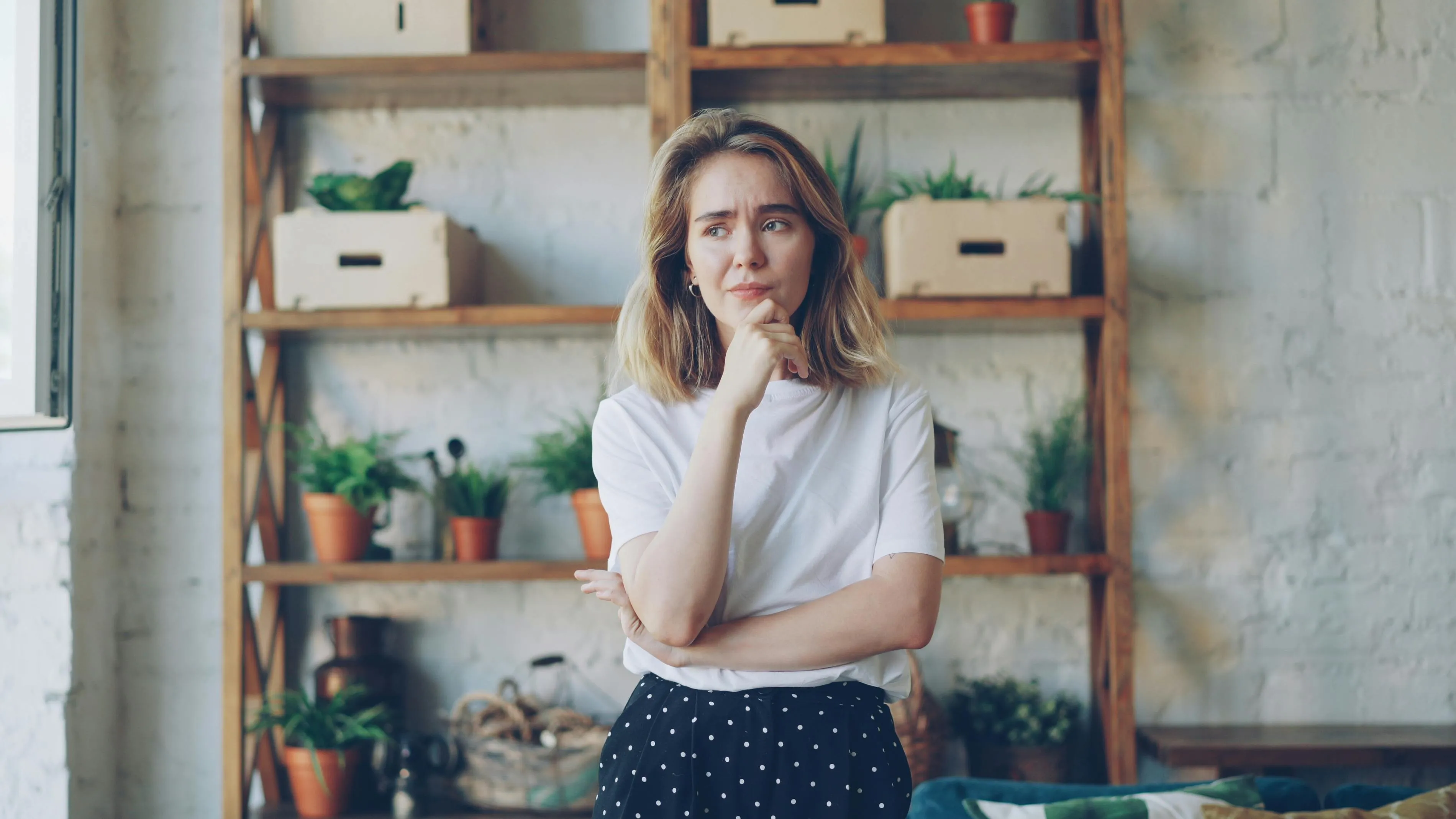 Young woman standing thoughtfully in a cozy room, reflecting on where her life would be set and big decision approach.
