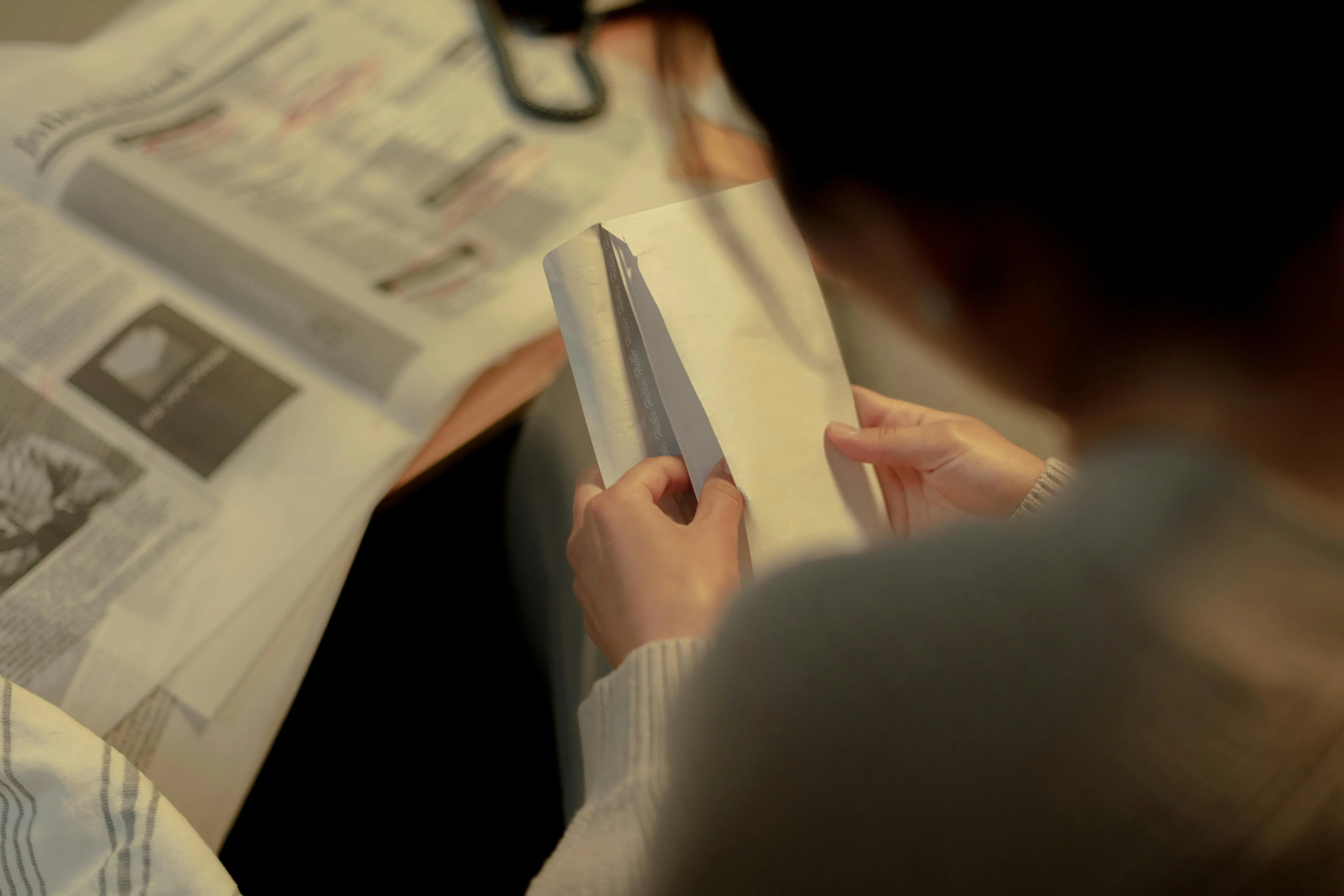 Person holding a mysterious envelope, sitting near a newspaper, contemplating where their life would be set next.