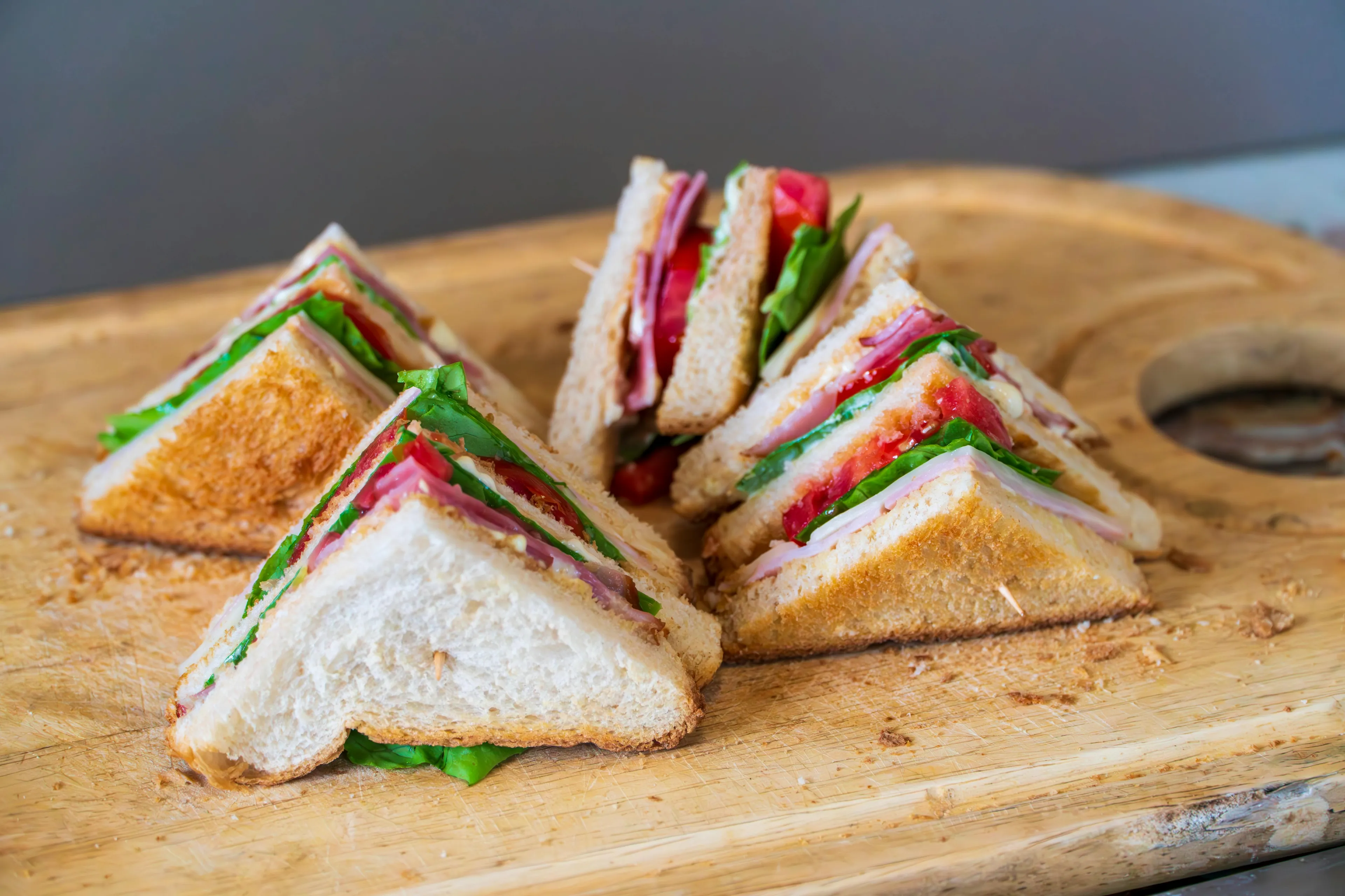 Triangle sandwiches with fresh sandwich filling including lettuce, tomato, and turkey on a wooden cutting board.