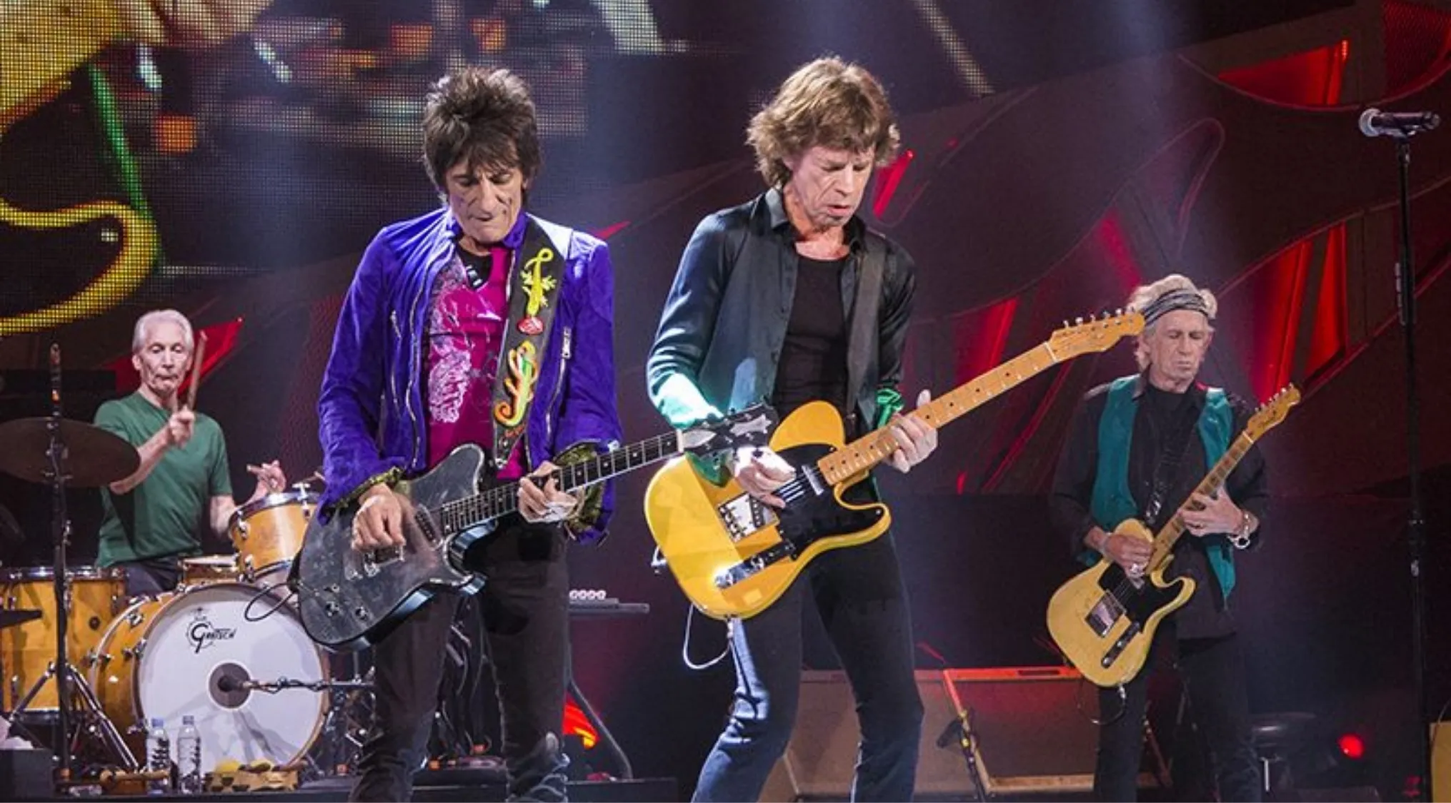 The Rolling Stones performing live on stage with guitars and drums during a vibrant concert show.