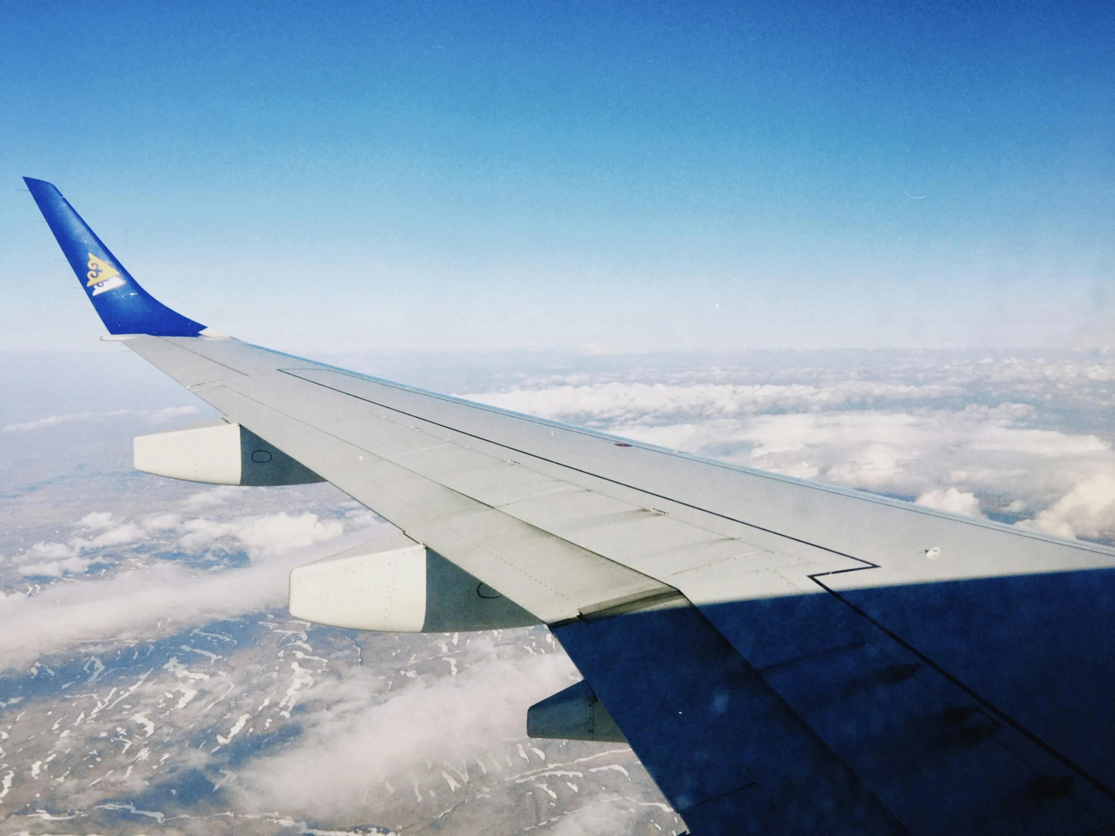 View from an airplane wing above clouds and mountains during a long flight, capturing the essence of air travel.