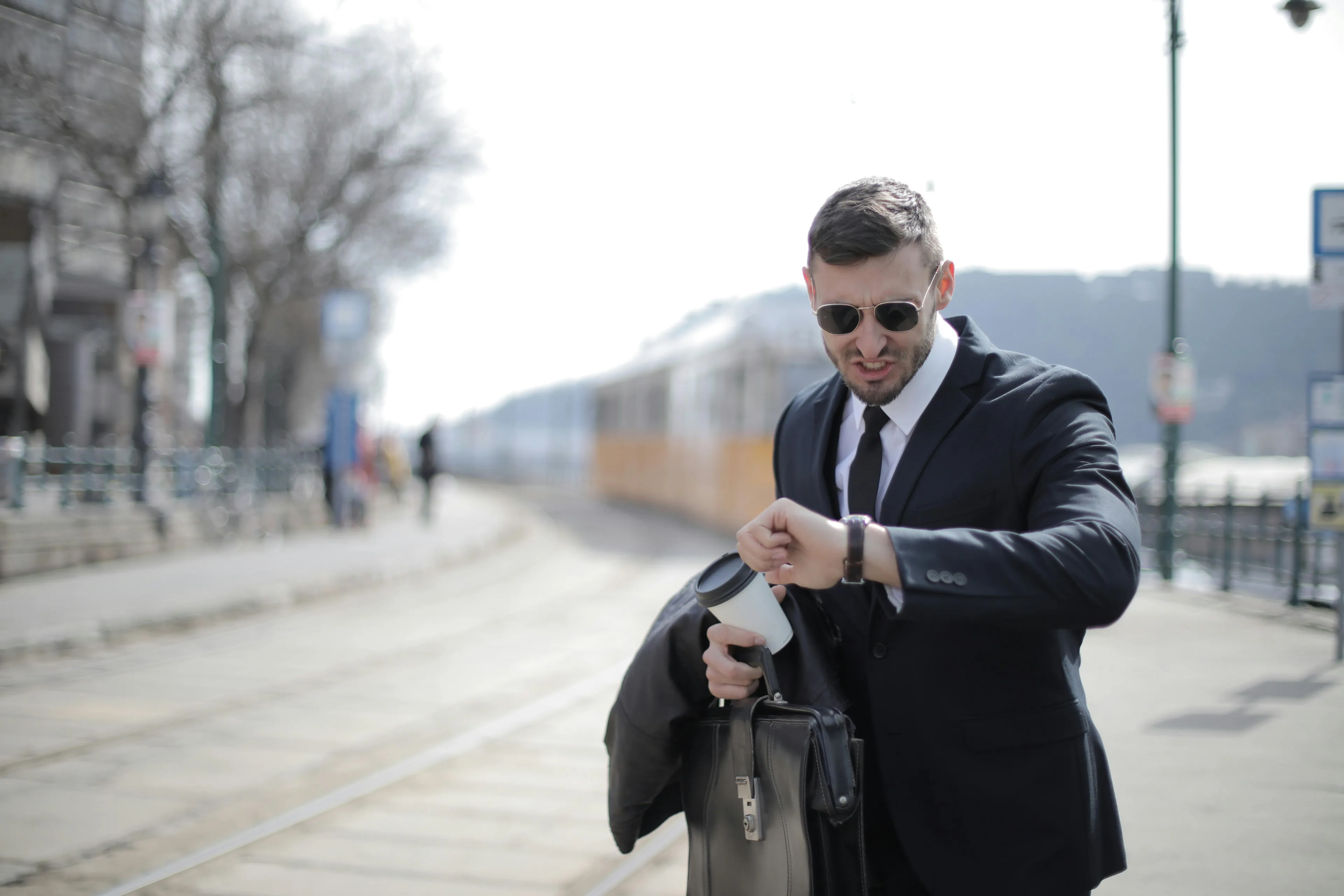 Man in suit checking watch on street next to train tracks, symbolizing life timing and excuses for being late.