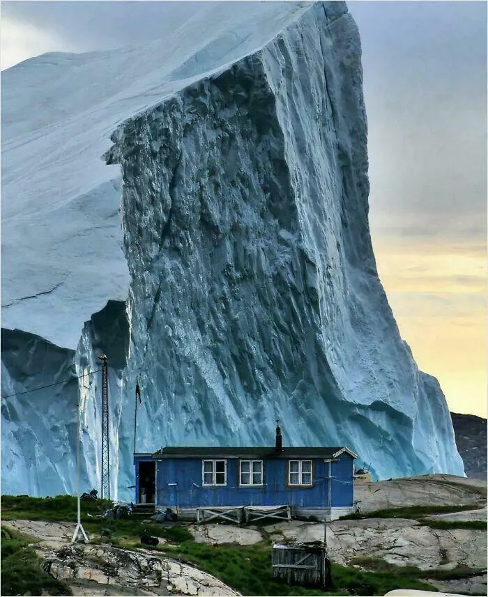 Iceberg Passing By House In Greenland