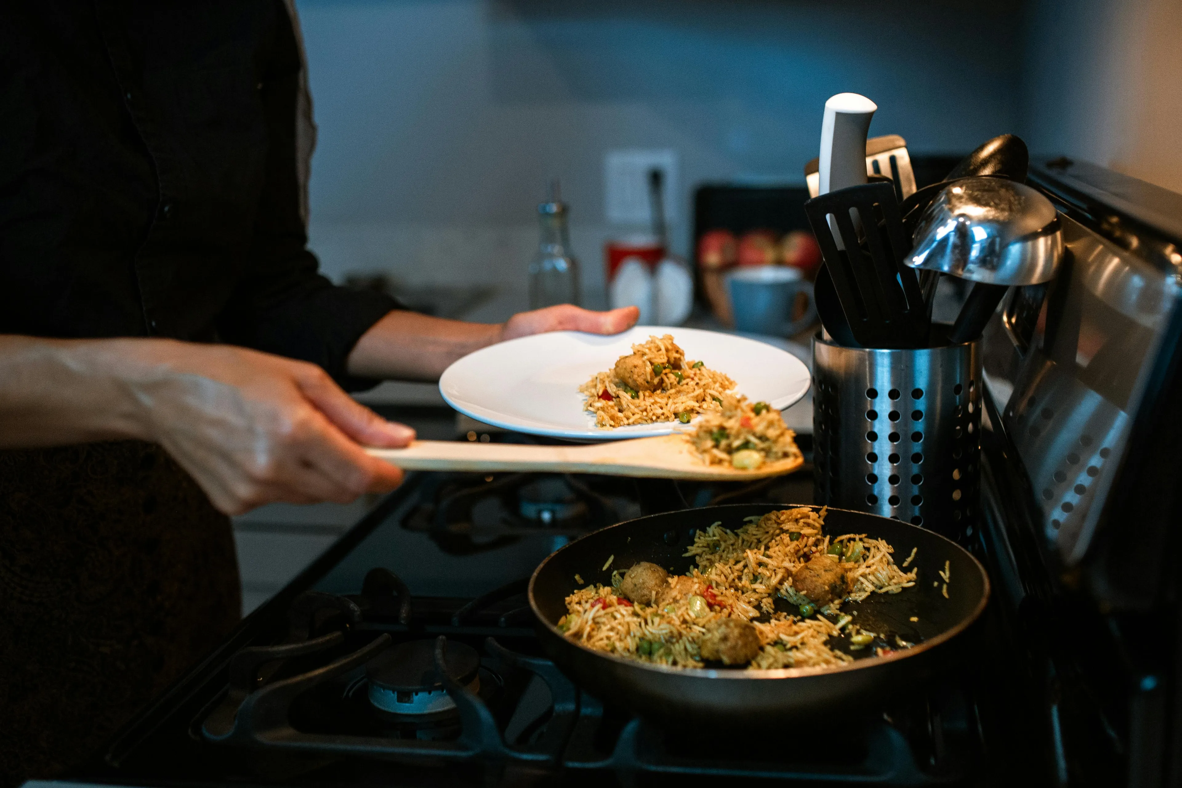Person cooking dinner and serving rice dish from pan on stove, exploring life setting and soundtrack while cooking.