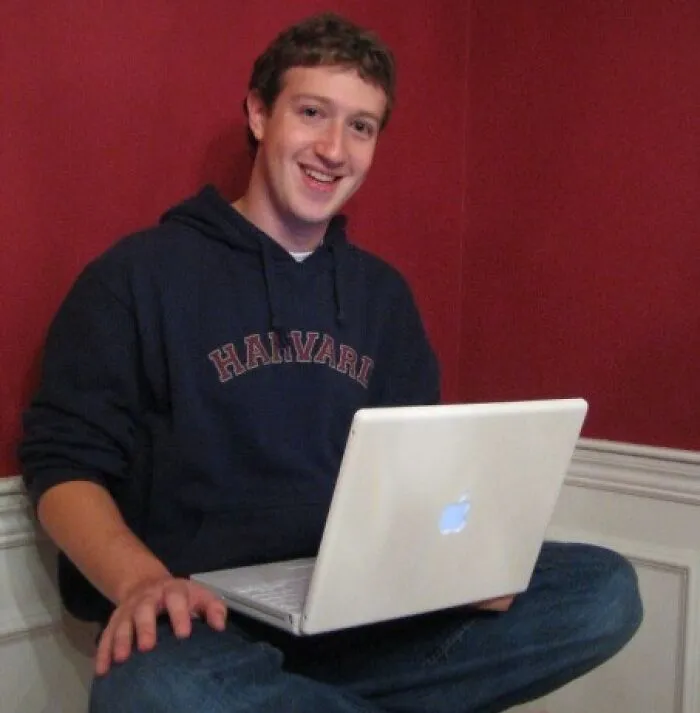 Young man wearing a Harvard hoodie using a white Apple laptop, representing milestones from the year you were born.