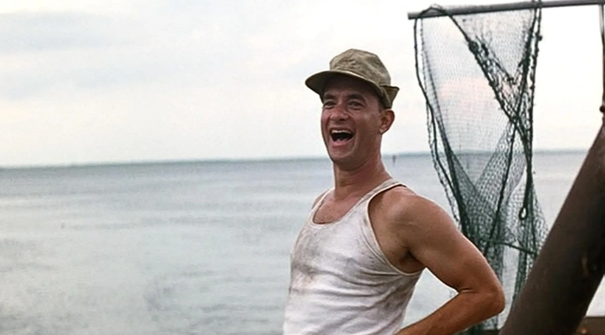 Tom Hanks smiling on a boat wearing a dirty white tank top and cap in a scene from a Best Picture Oscar-winning film.
