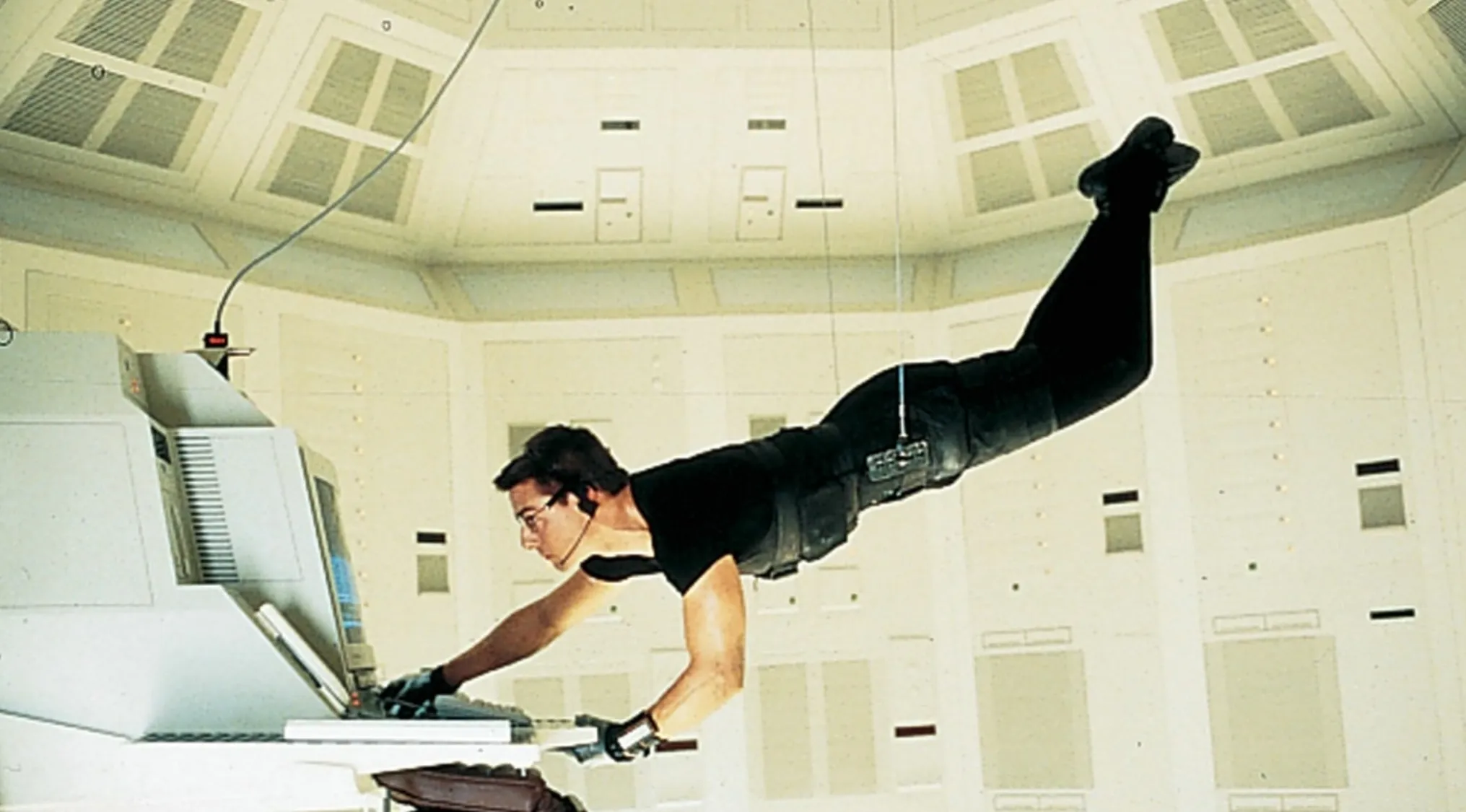 Man in black outfit suspended mid-air typing on computer in a tense scene from a movie quiz challenge.