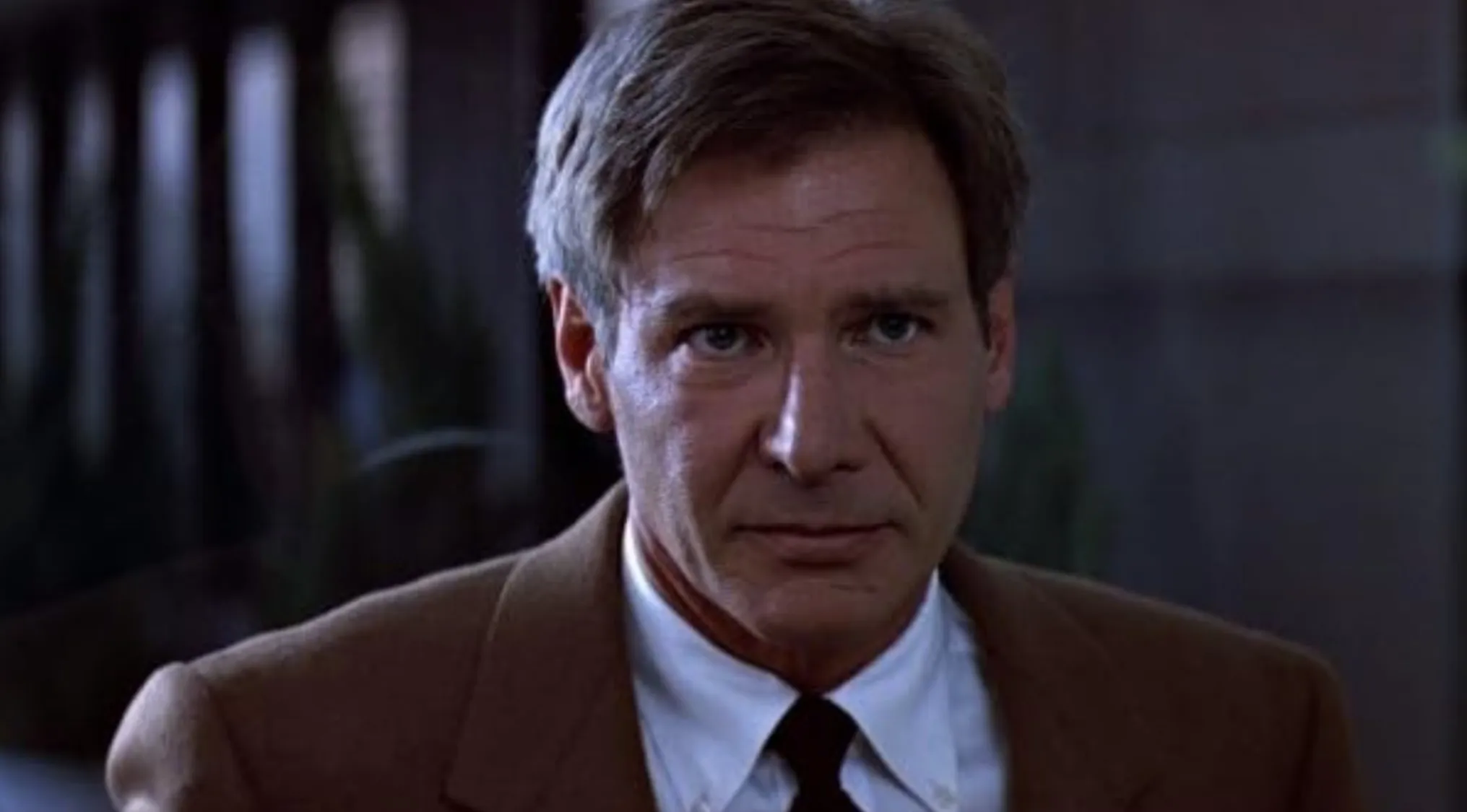 Harrison Ford close-up in brown suit and tie in a dimly lit indoor setting