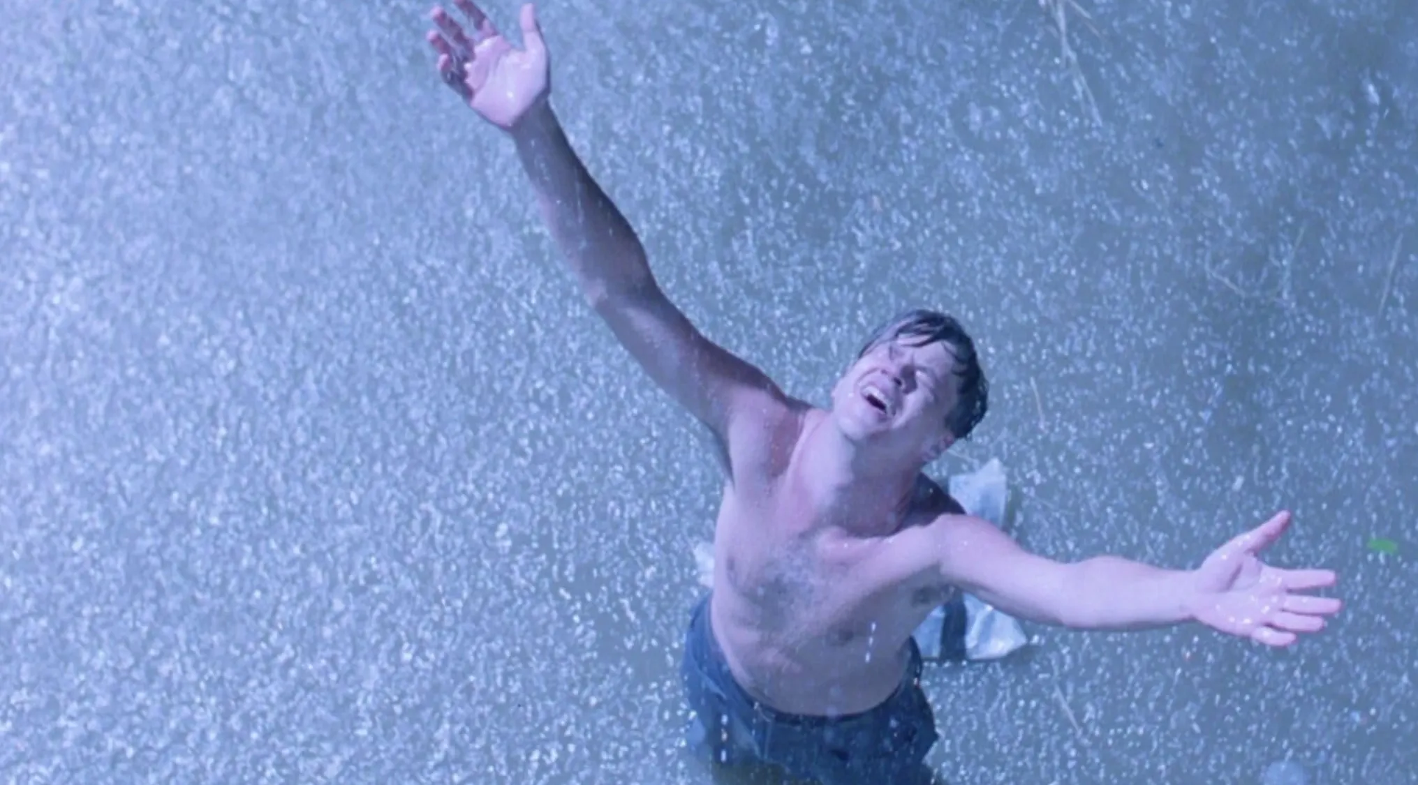 Man with open arms standing in rain in a memorable scene from a popular 90s film in the ultimate movie quiz.
