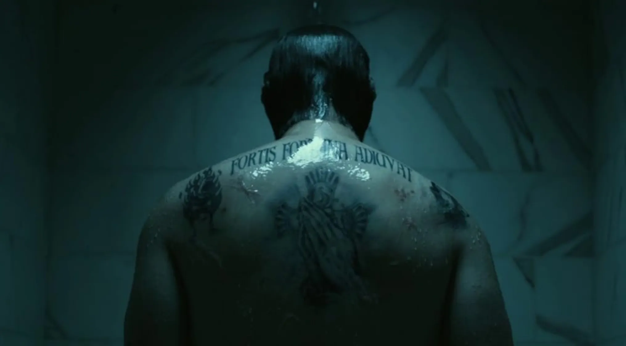 Back view of John Wick with prominent tattoos on his wet back in a dimly lit shower scene from the action movie franchise John Wick.