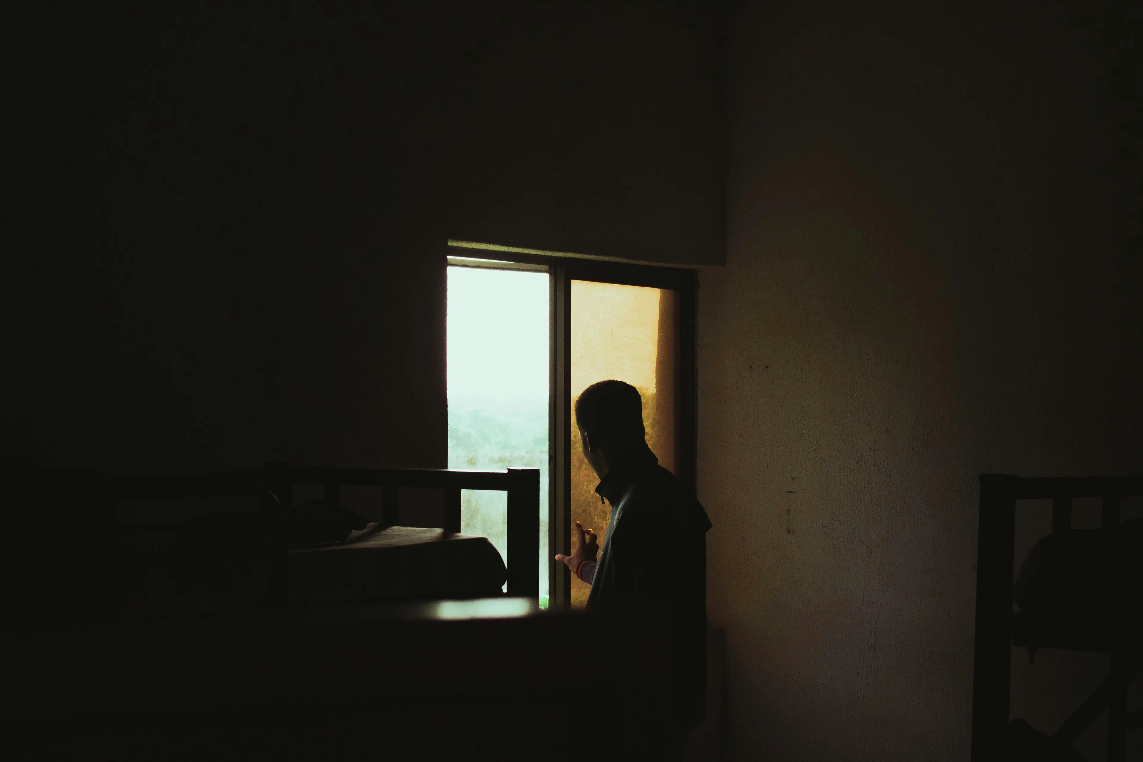 Silhouette of a person near a window in a dark room during a power outage evening, reflecting quietly alone.