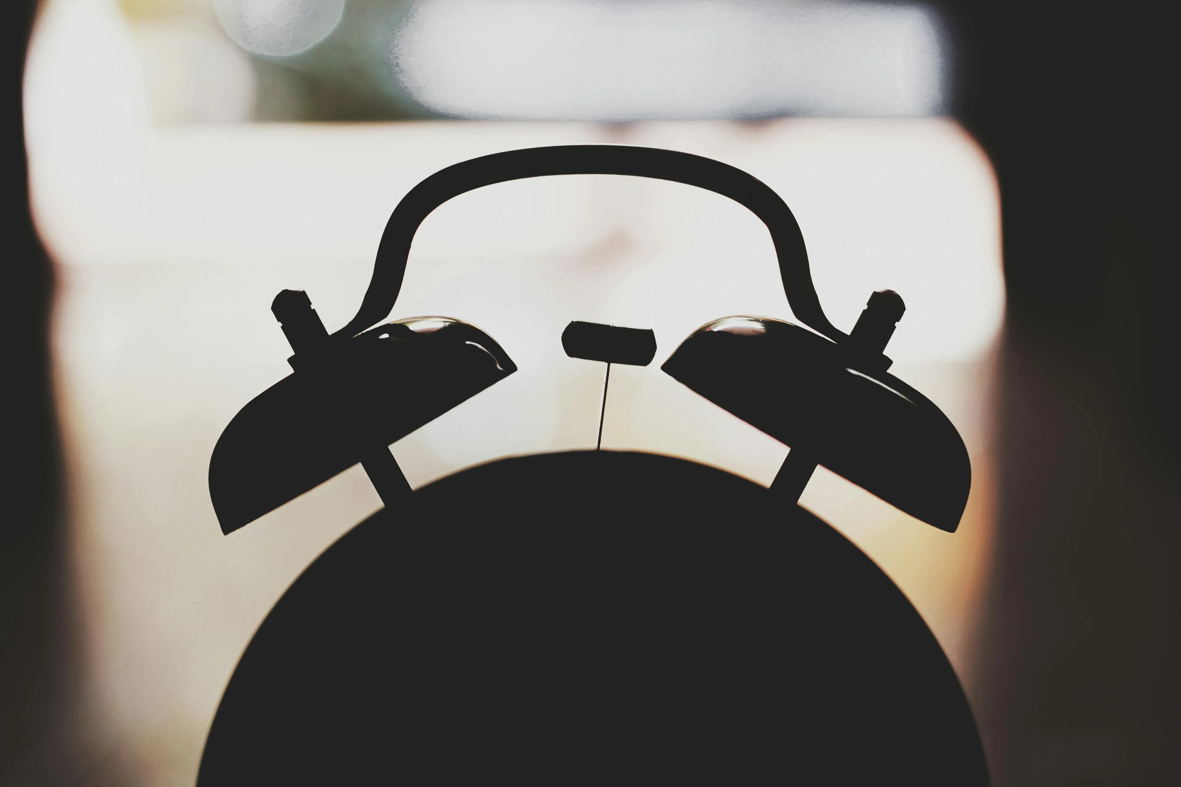Close-up silhouette of an old-fashioned alarm clock representing the morning alarm sound you pick.