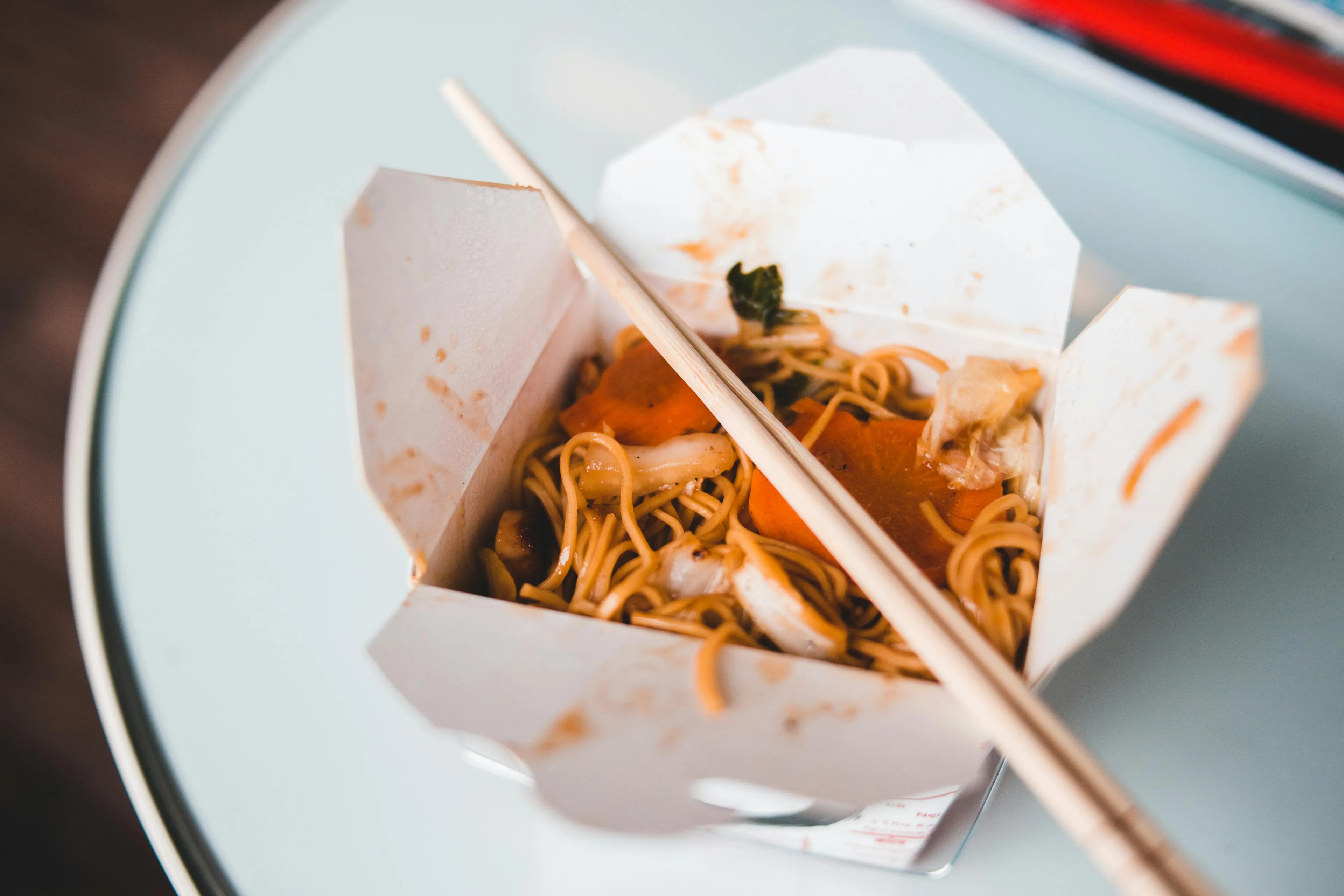Takeout noodles with chopsticks on a plate, representing how do you handle leftovers in daily life.
