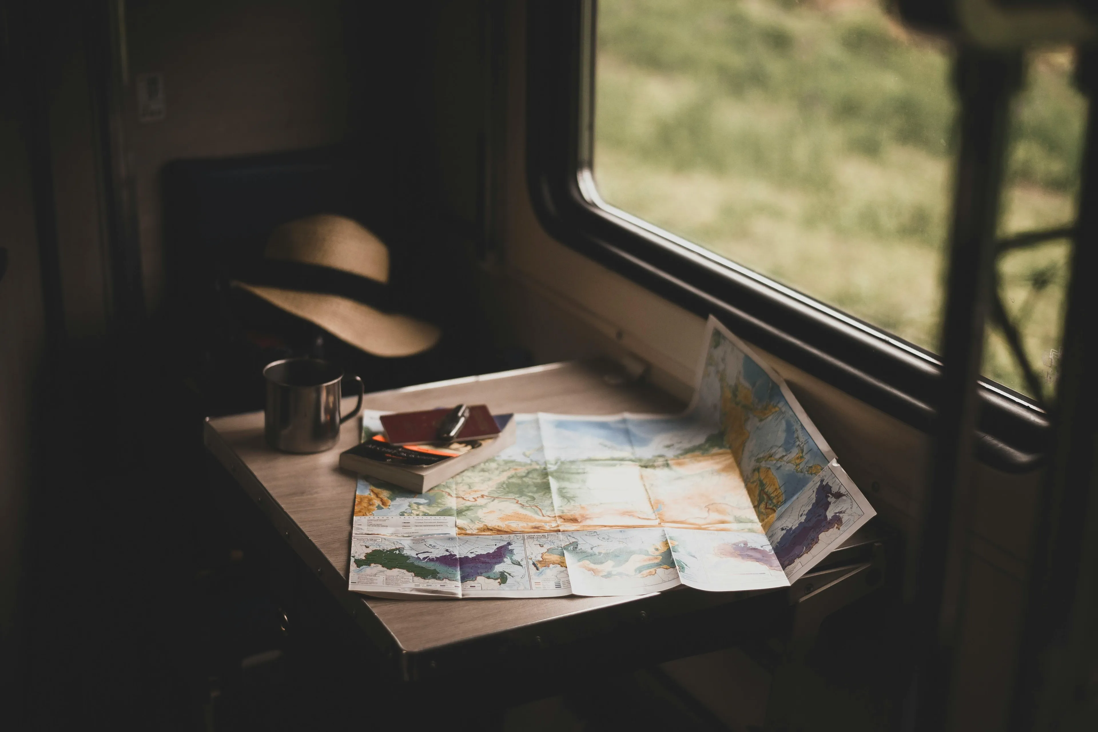 Map and travel journal on a train table by the window, suggesting planning next trip on a relaxing Saturday.