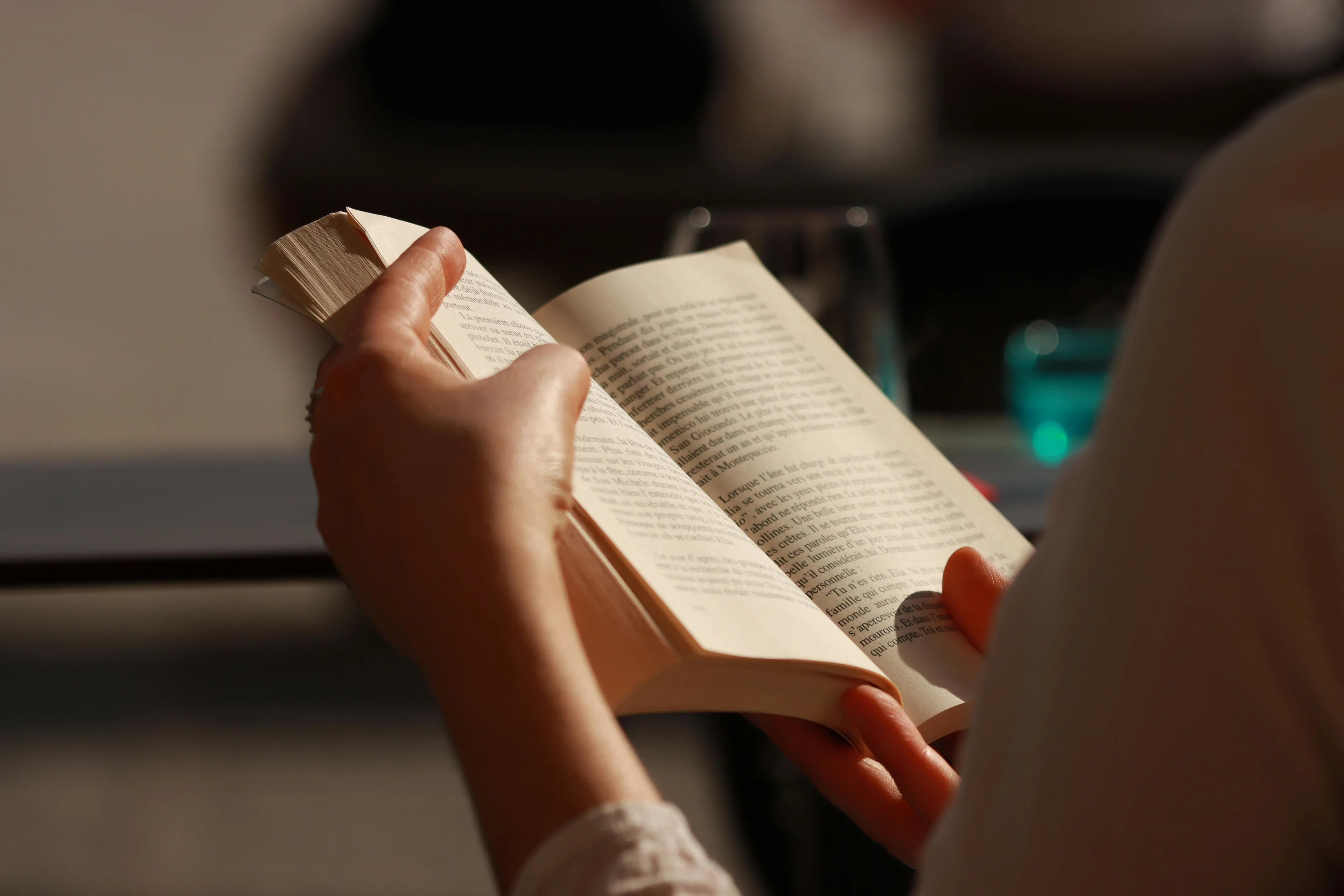Person reading a book with focused hands holding pages, enjoying a quiet Saturday activity in warm natural light.