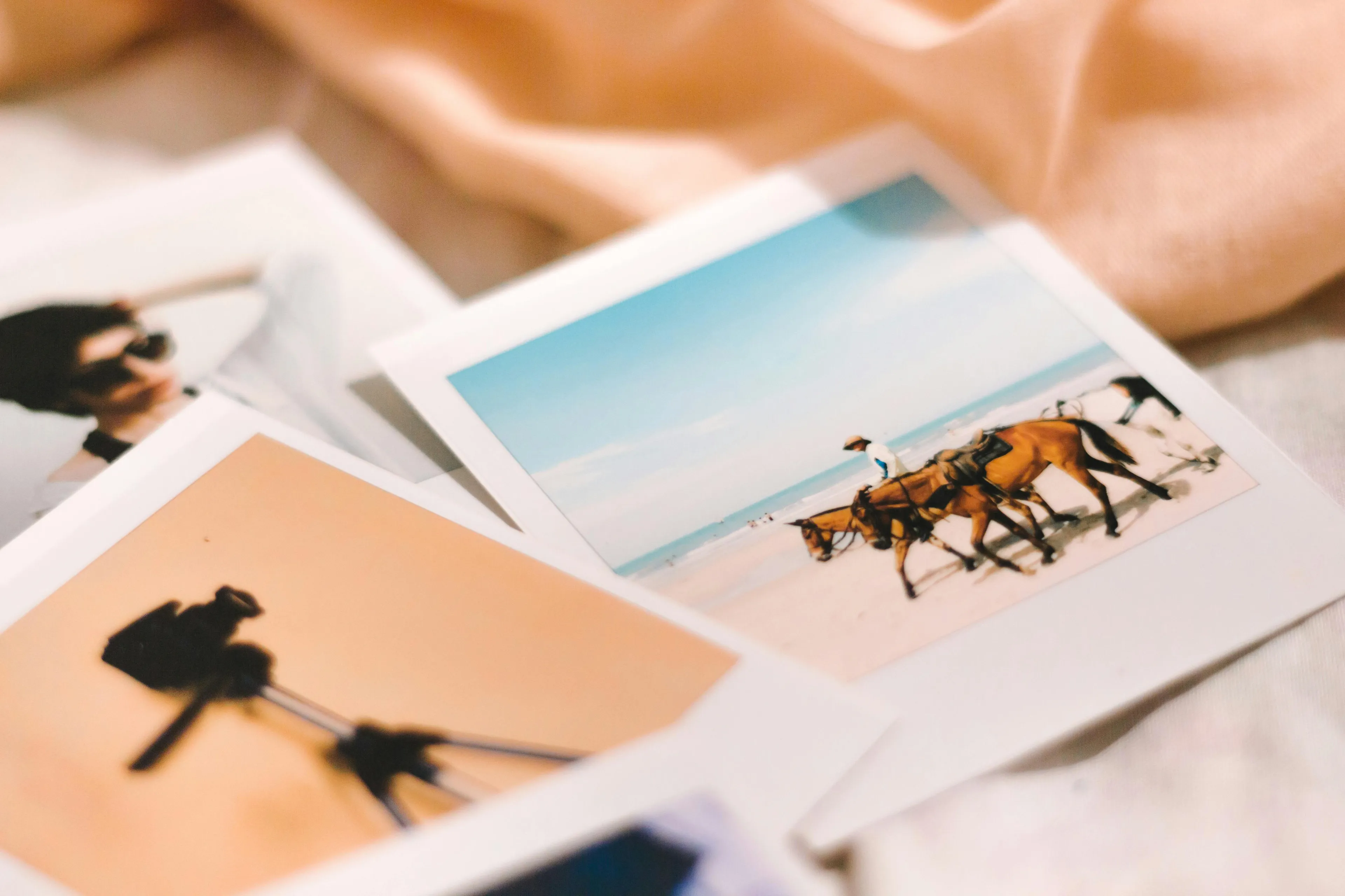 Old photos scattered on a soft surface, featuring a beach scene with horses and a person, perfect for sorting through memories.