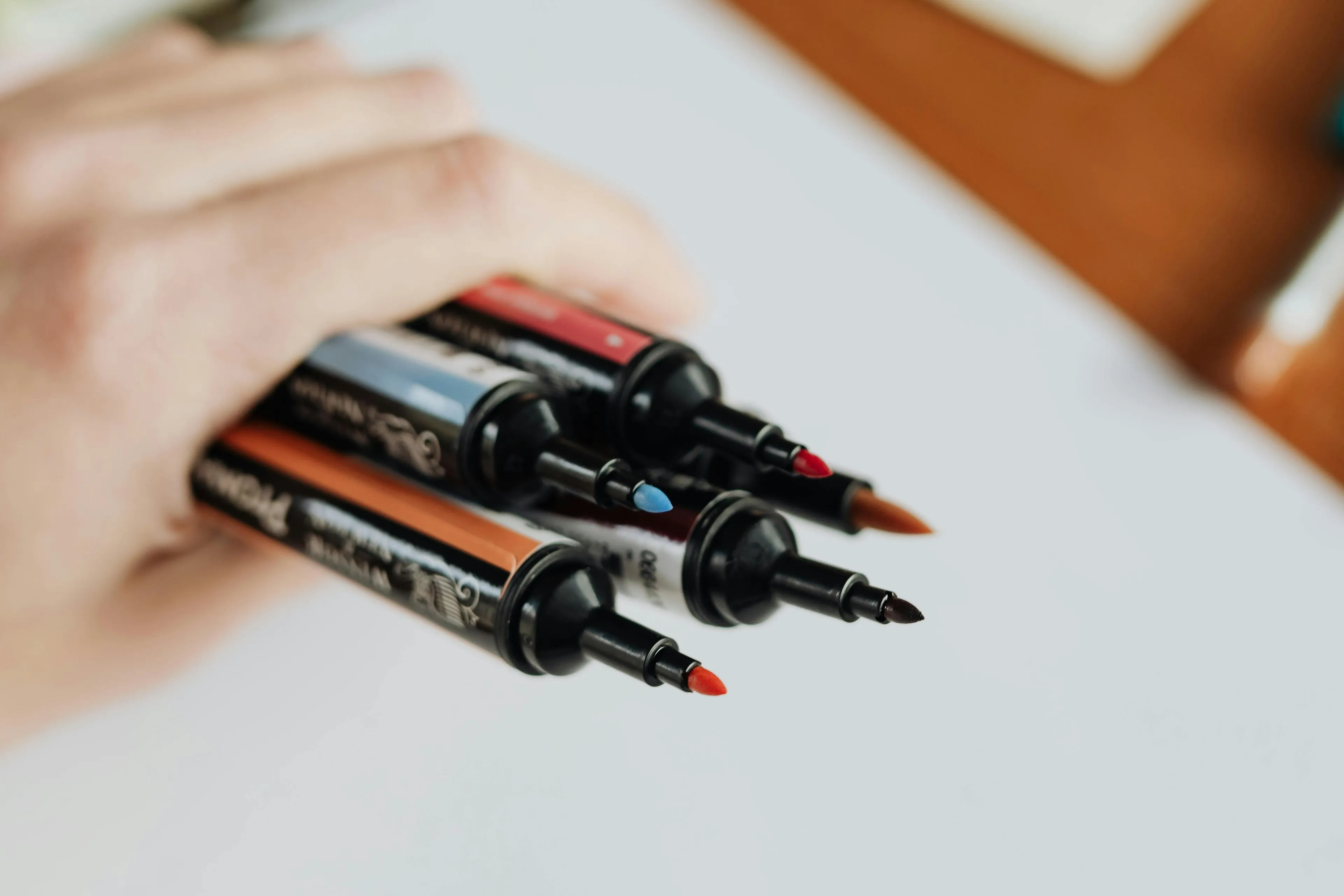 Hand holding a fresh pack of markers with colorful tips ready to use on a plain white surface.