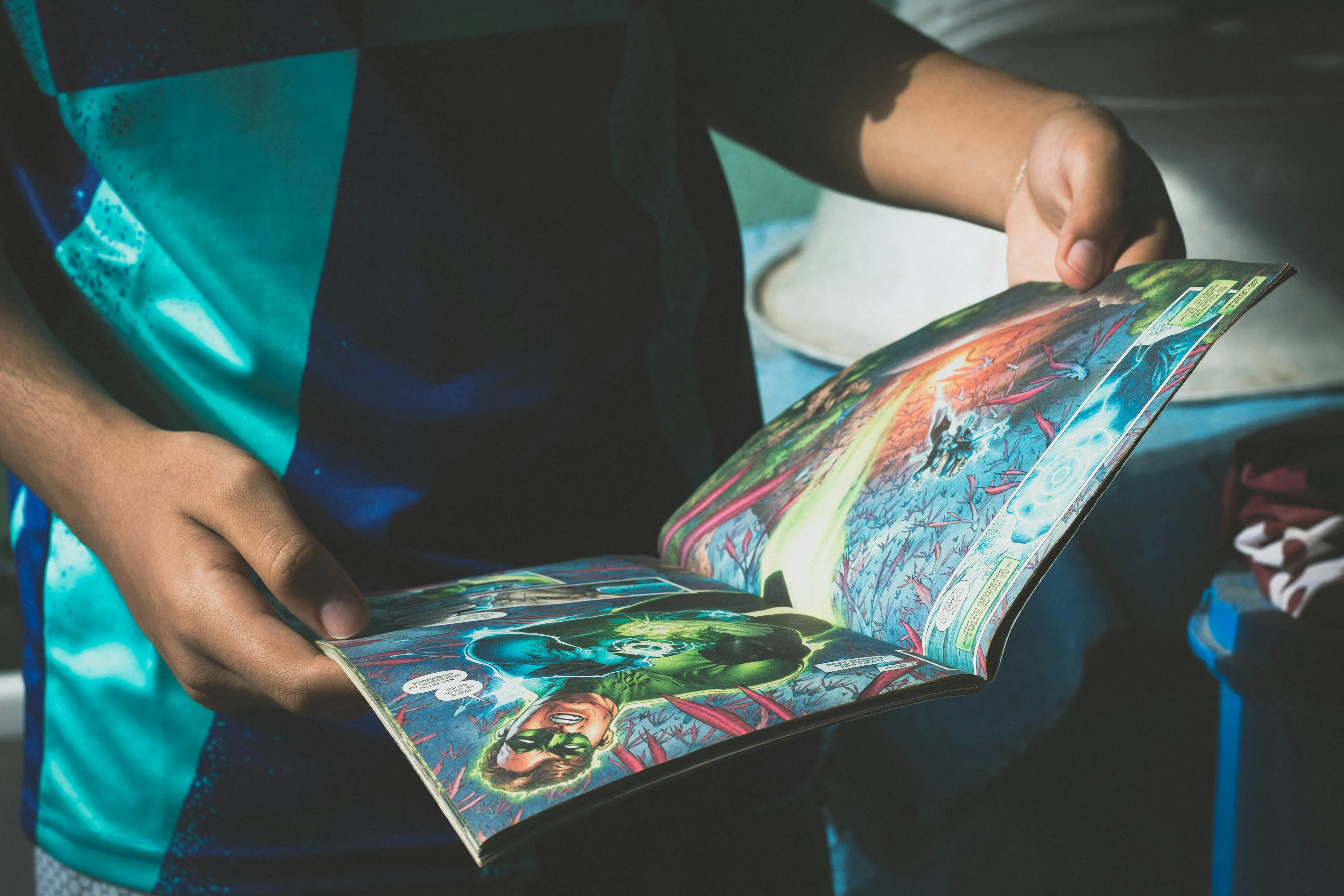 Person holding new comic book pages with colorful superhero illustrations in bright natural light outdoors.