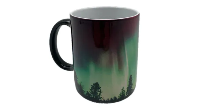 Color-changing coffee mug displaying a nature-inspired pattern with trees and an aurora-like effect on its surface.