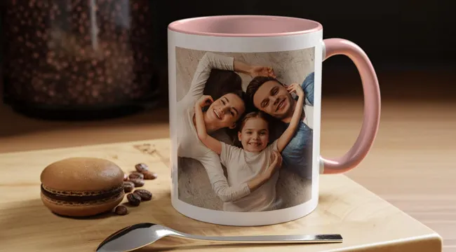 Coffee mug with a family photo print featuring smiling parents and child on a wooden tray with a macaron and coffee beans.