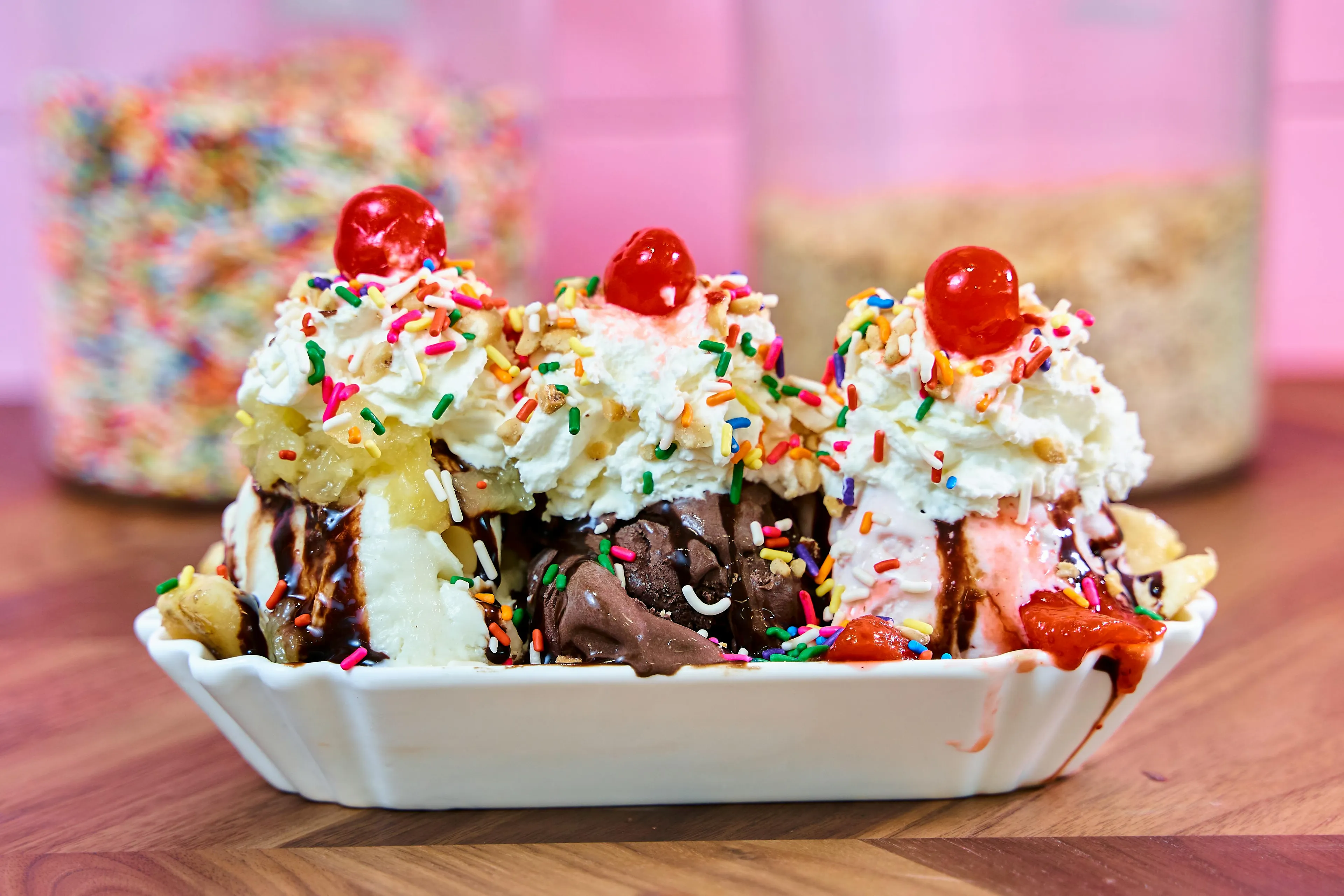 A colorful sundae with whipped cream, sprinkles, cherries, chocolate syrup, and banana slices in a white dish.
