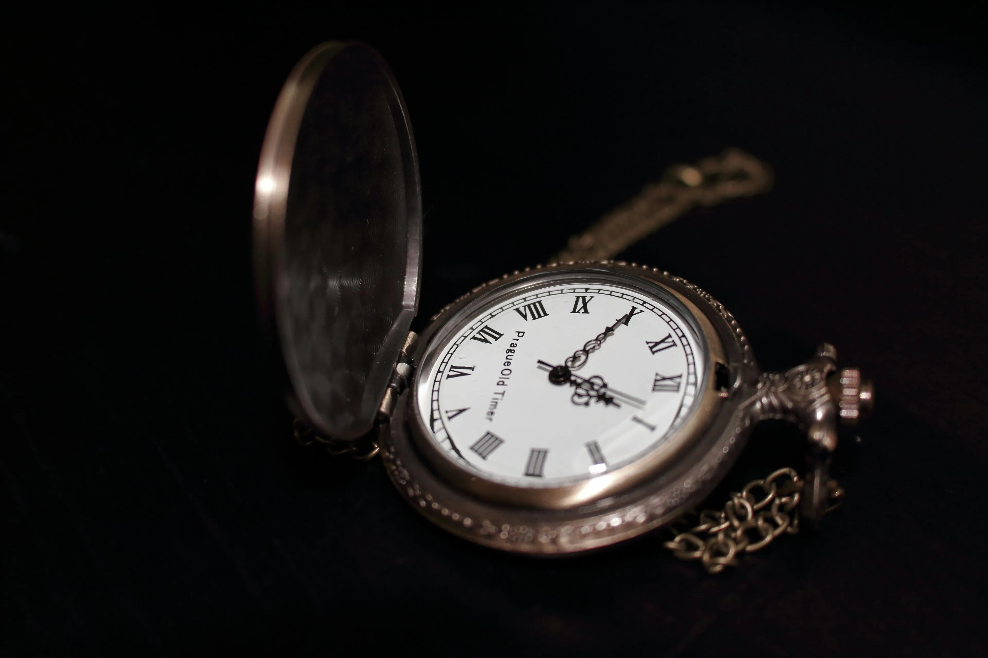 An old vintage pocket watch with an open cover resting on a dark surface, showing Roman numeral clock face.