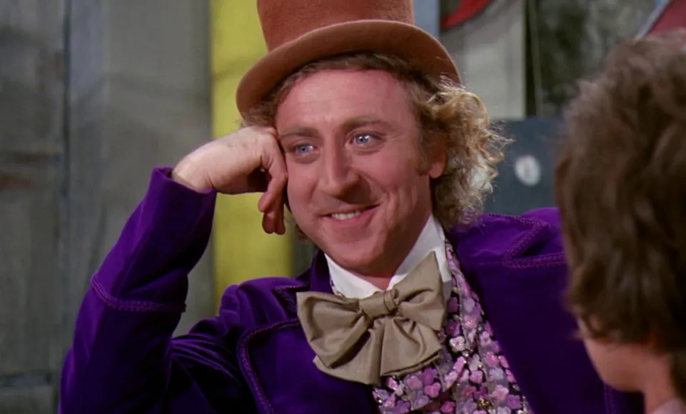 Willy Wonka in a purple coat and top hat smiling warmly, a classic scene from the childhood comfort movie.