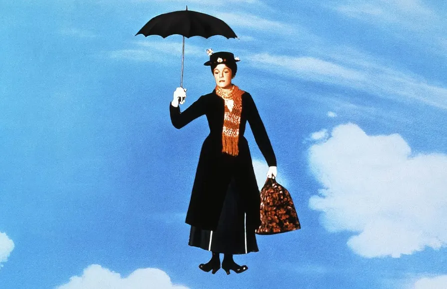 Mary Poppins dressed in black coat and hat, holding an umbrella, floating against a bright blue sky with clouds.