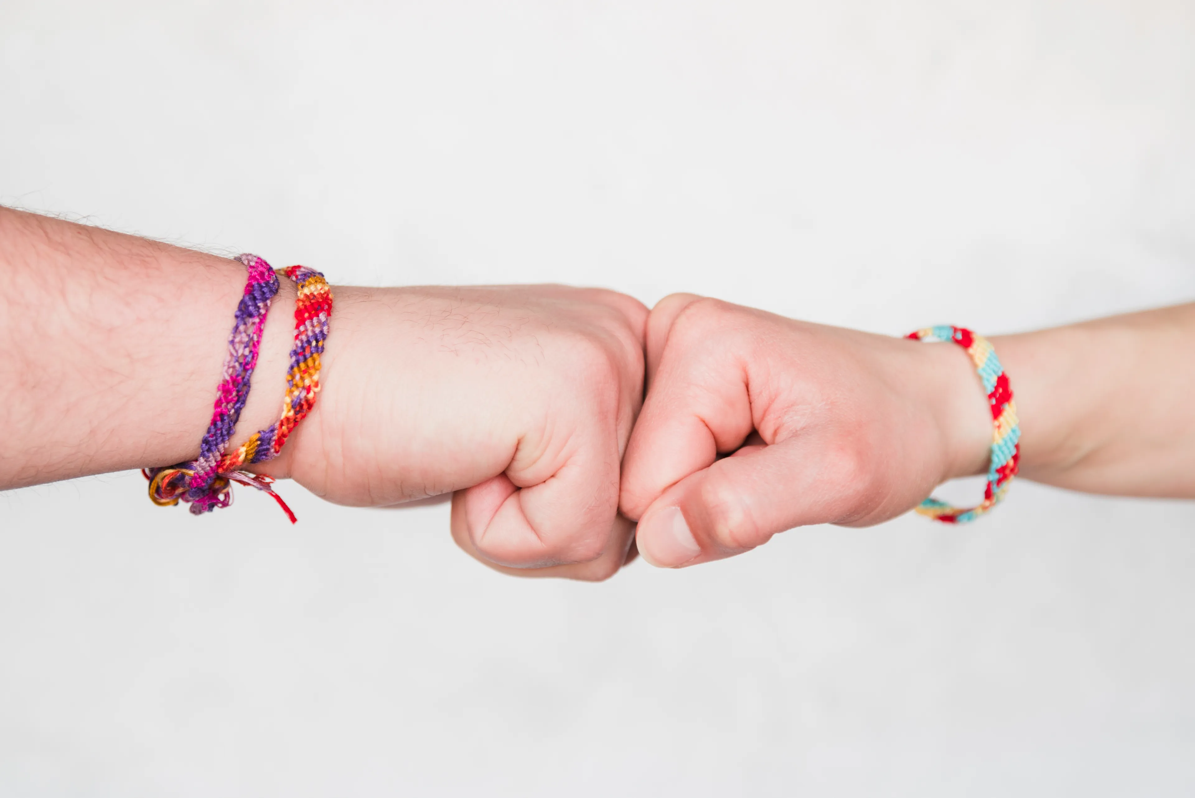 Two hands wearing colorful friendship bracelets bumping fists against a plain white background.