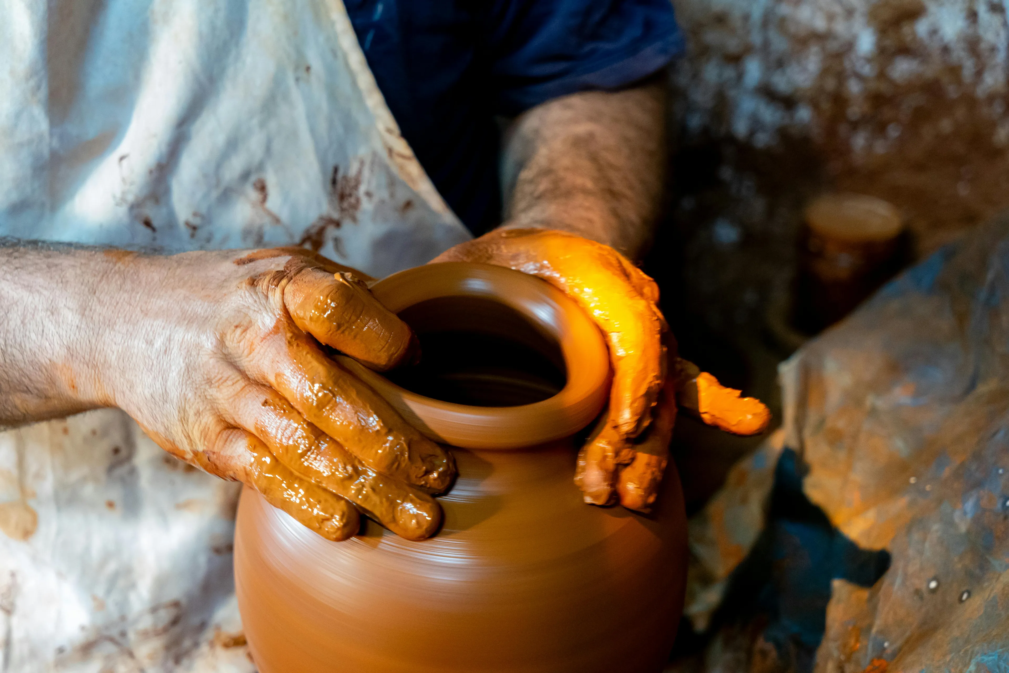 Hands shaping a clay pot on a pottery wheel, showcasing the art of childhood craft projects with wet clay.