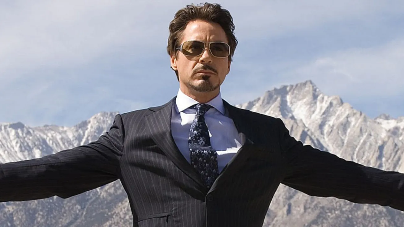 Tony Stark in a suit and sunglasses with arms outstretched against a mountainous backdrop.