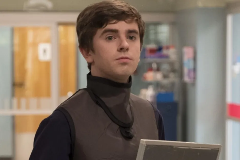 Young man in a hospital setting wearing a protective vest, holding a clipboard, related to The Good Doctor TV show.