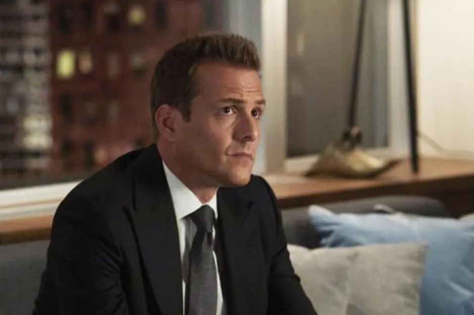 Man in a black suit and tie sitting indoors on a couch, featured in the show Suits.
