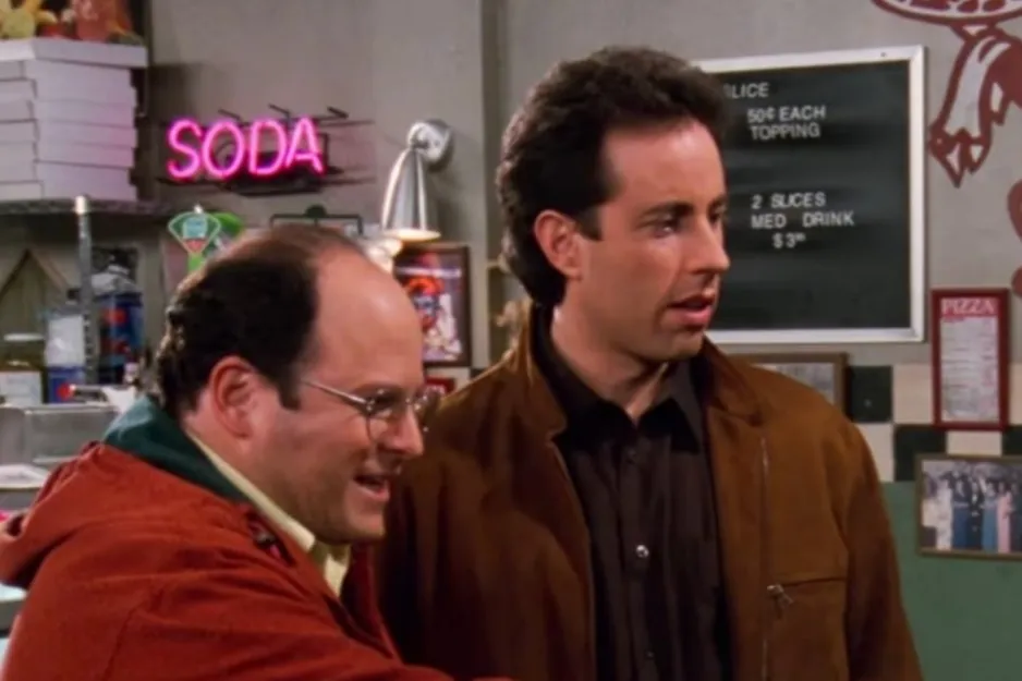 Scene from Seinfeld featuring two men in a casual setting with a neon soda sign in the background.