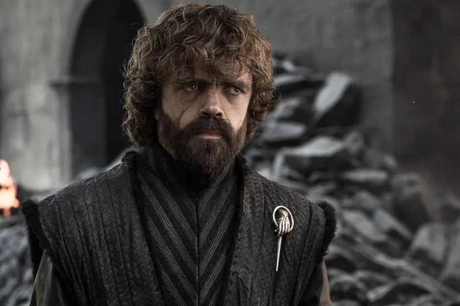 Tyrion Lannister from Game of Thrones wearing dark medieval-inspired clothing with a Hand of the King pin.