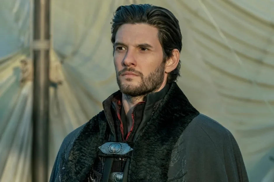 Man in dark medieval costume from Shadow and Bone standing outdoors with a serious expression and a blurred background.