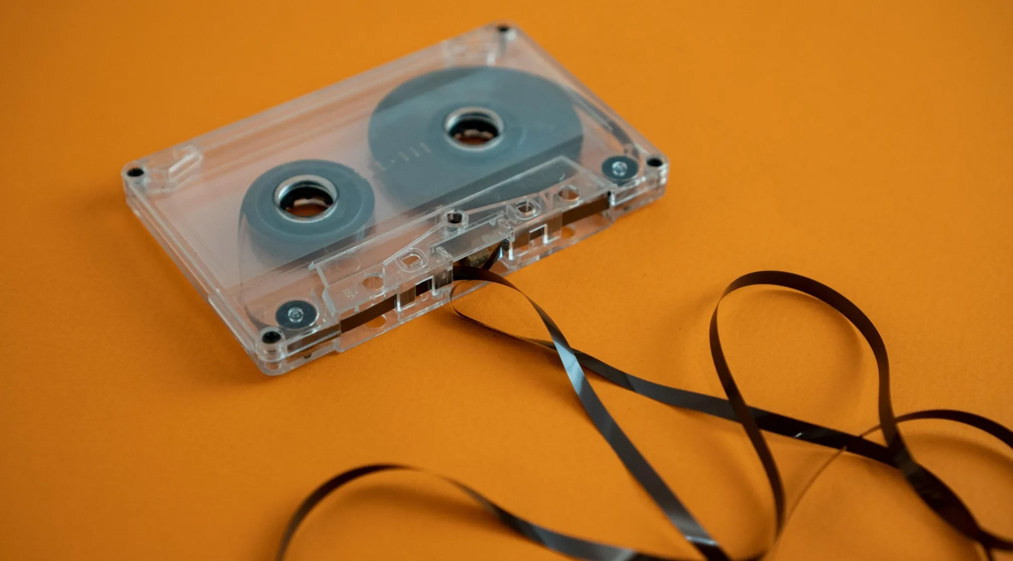 Clear cassette tape with unwound black tape resting on an orange background representing pre-2000s TV shows and sitcoms.