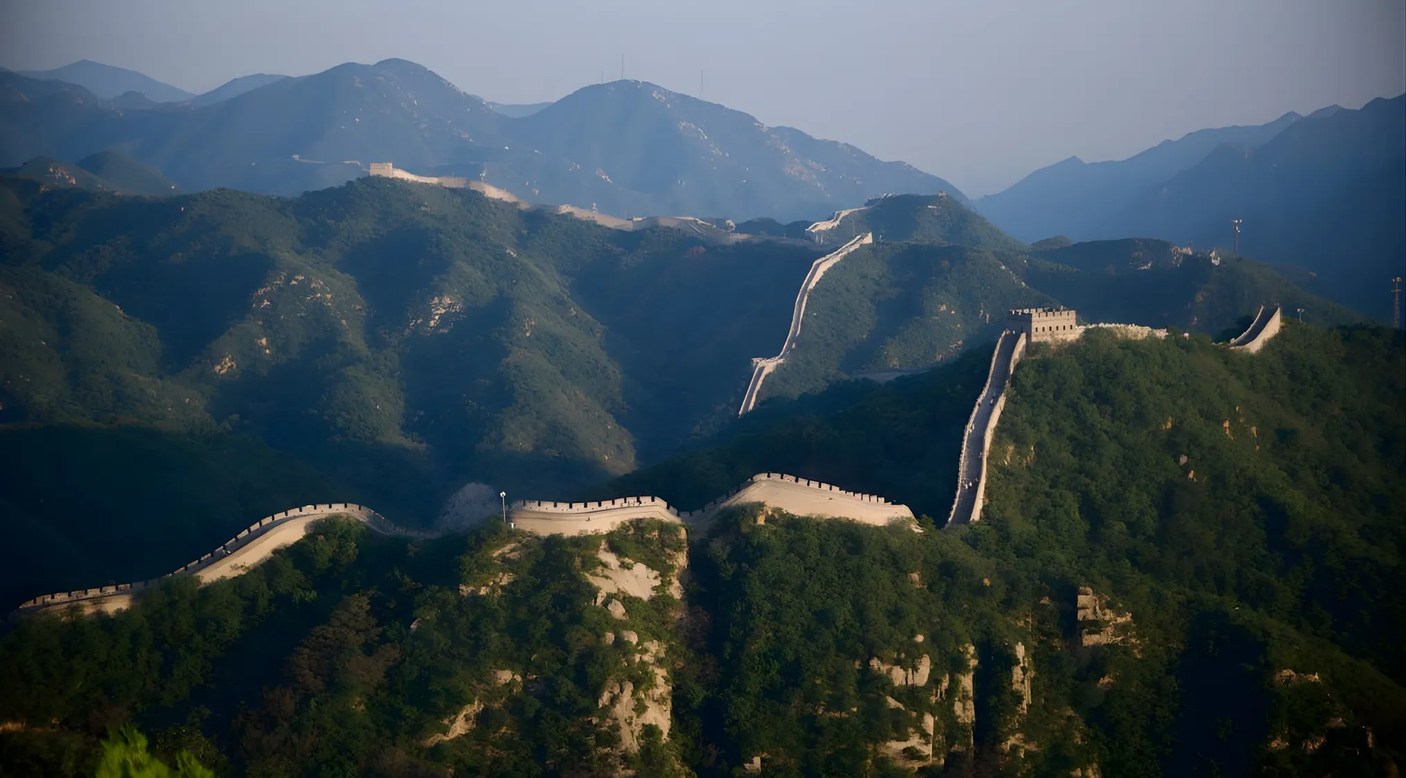 Great Wall of China winding through mountainous terrain under clear skies, showcasing its vast historic structure.