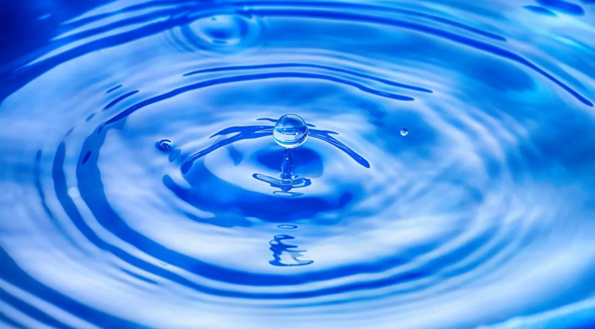 Close-up of a water droplet creating ripples in blue water illustrating science and myth about boiling and freezing.