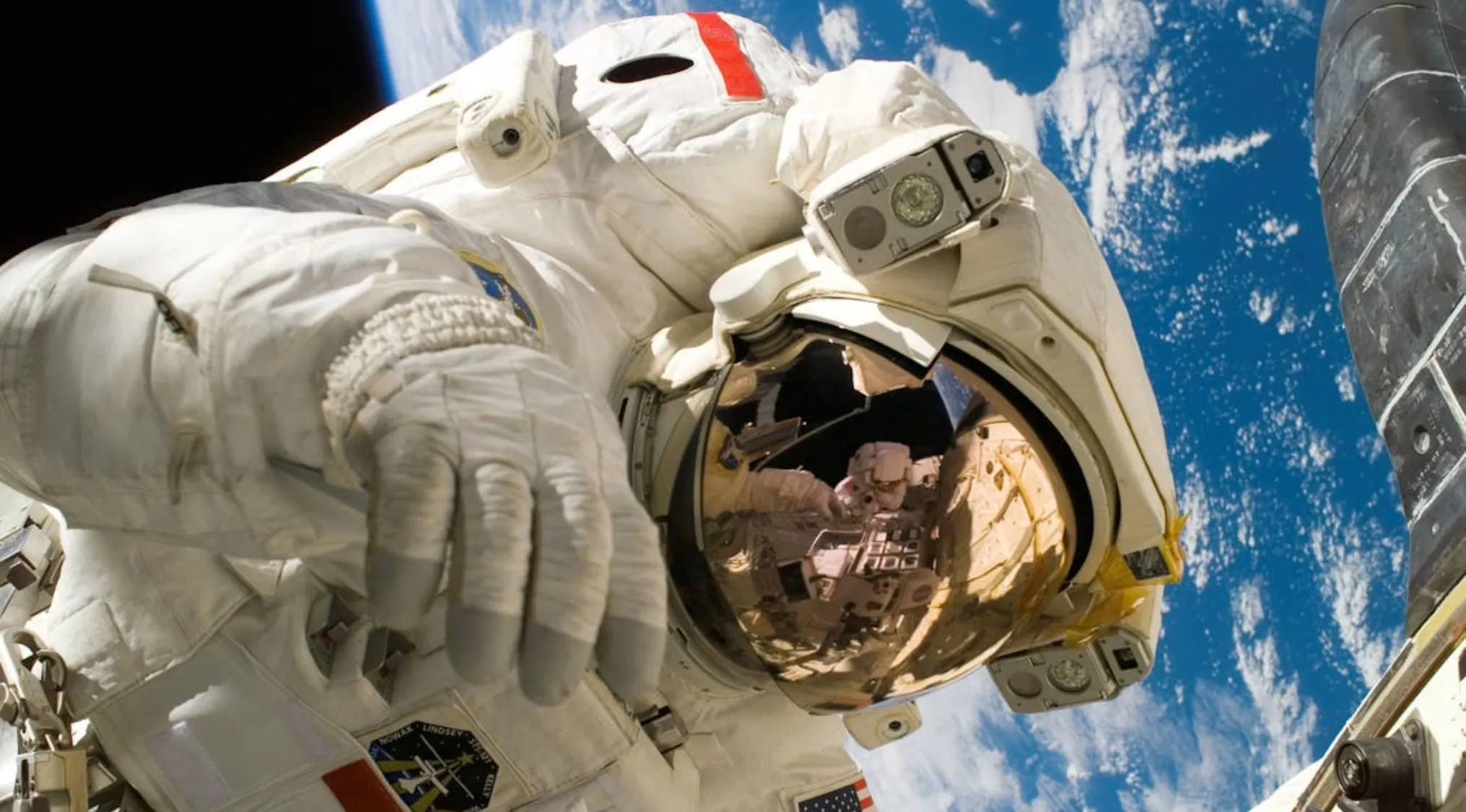 Astronaut in a white space suit floating outside a spacecraft with Earth visible in the background.