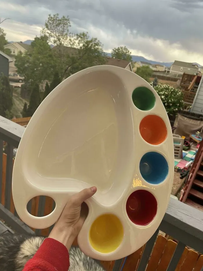 A hand holding a white artist's palette shaped plate with colorful dips, a fun thrift store jackpot.