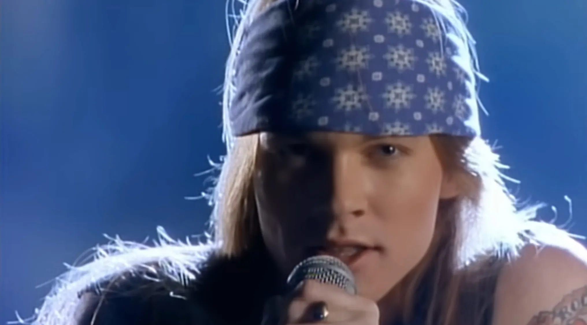 Lead singer wearing a bandana singing into a microphone in a music challenge identifying bands from frontmen.